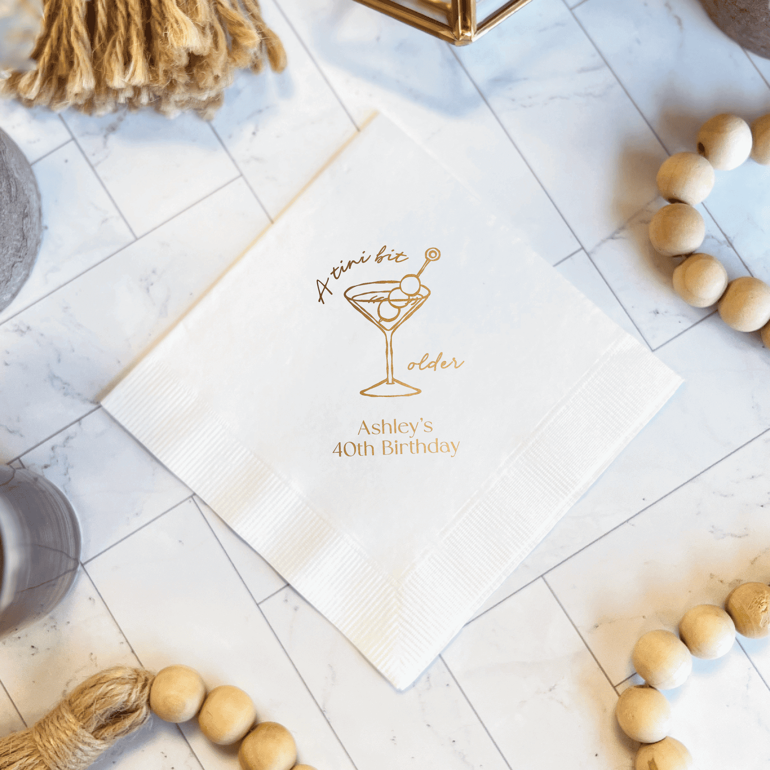 White napkin with gold foil martini glass design and personalized text reading "cheers to 40 adler 40th Birthday"