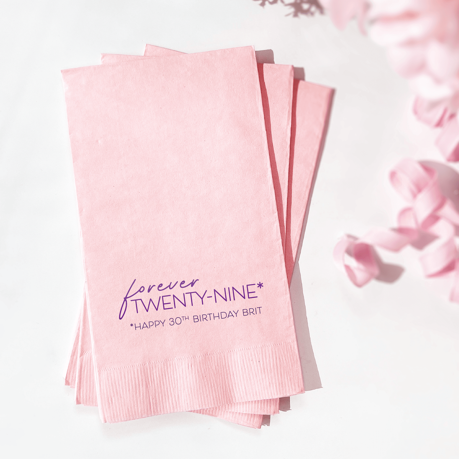Stack of blush pink napkins with burgundy foil-stamped text reading "Forever Twenty-Nine" and "Happy 30th Birthday Britt"