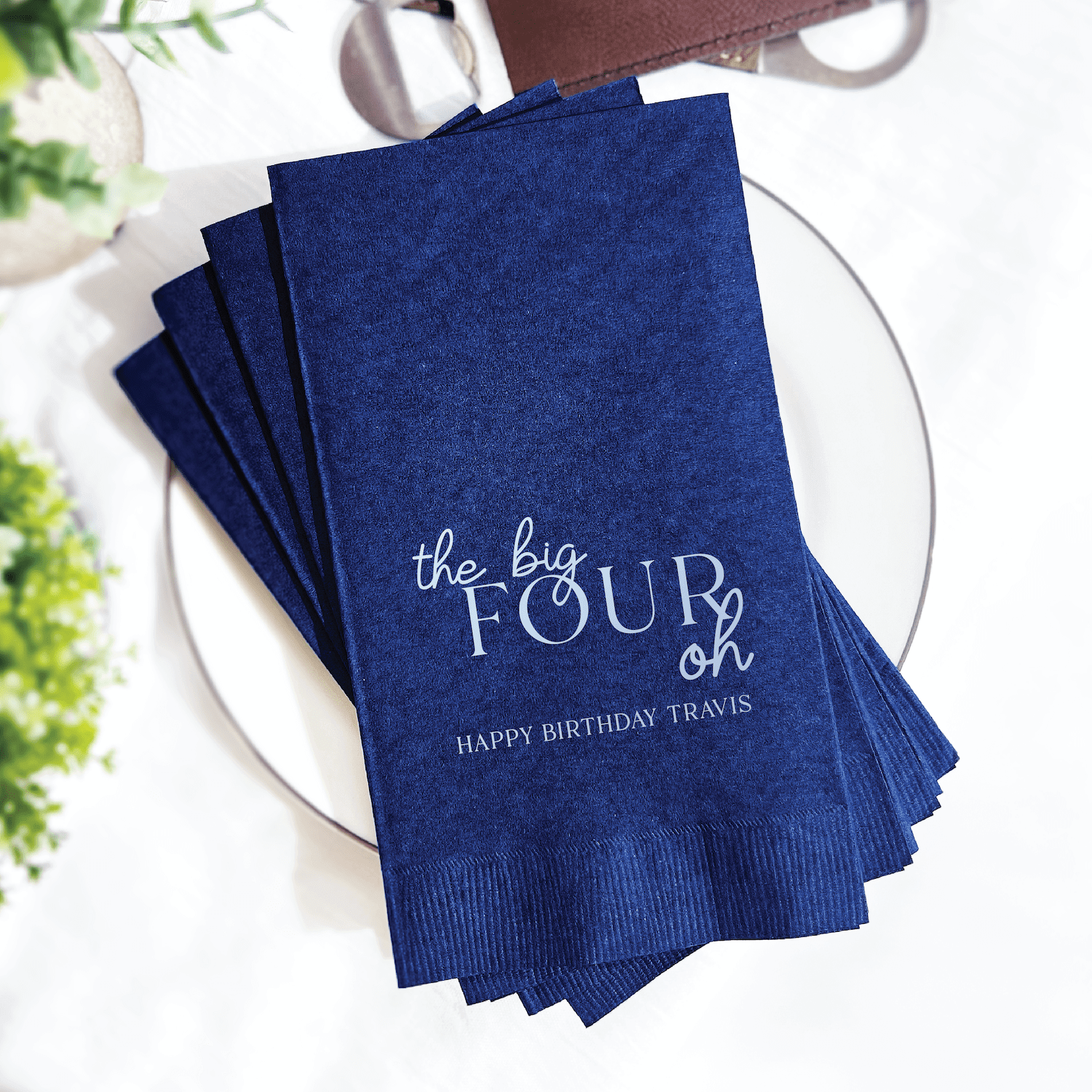 Navy blue foil-stamped napkins with "the big FOUR oh" and "HAPPY BIRTHDAY TRAVIS" printed in white text.