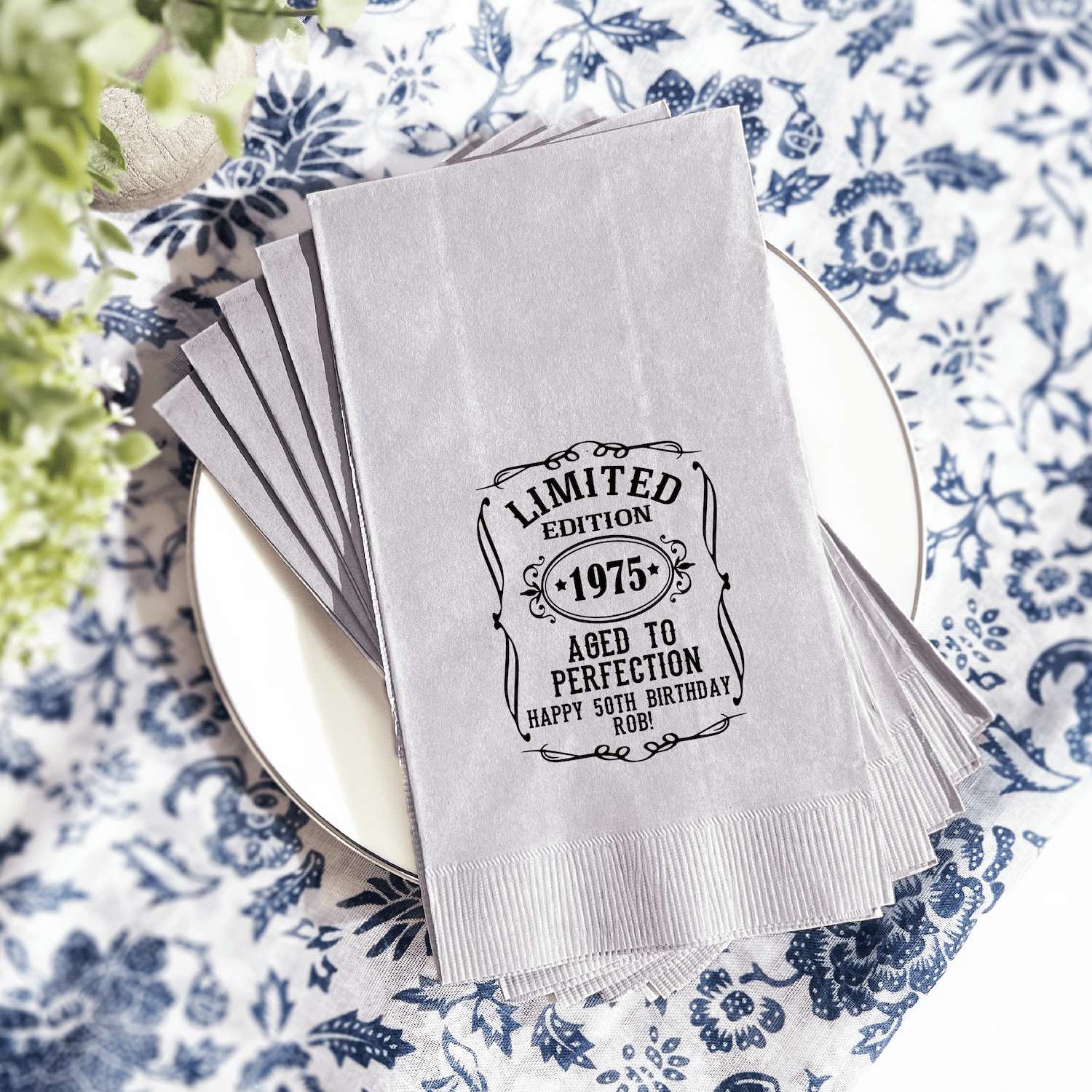White napkins with black foil-stamped "Limited Edition 1975 Aged to Perfection" design, stacked on white plate.
