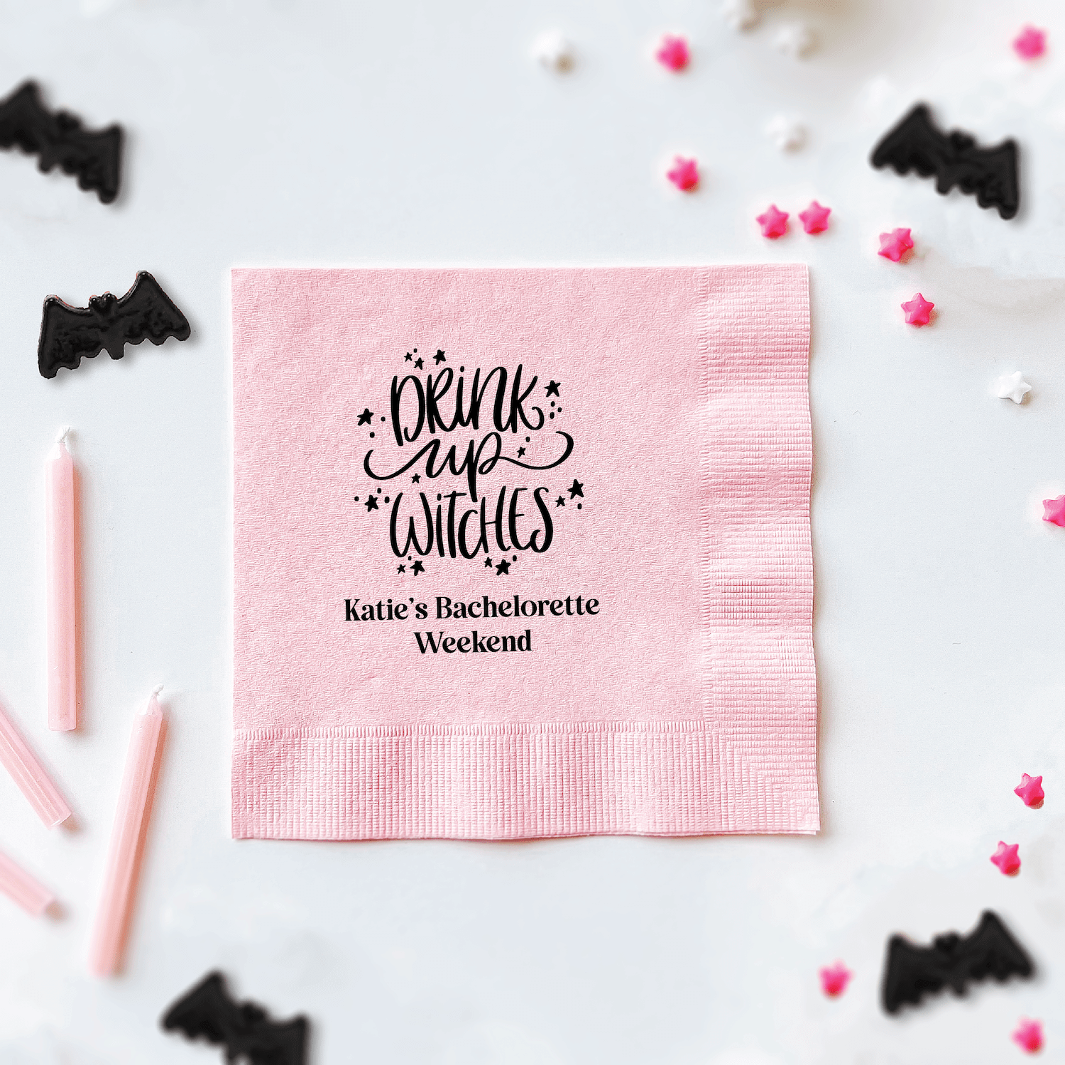 Pink cocktail napkin with "Drink Up Witches" text and personalized "Katie's Bachelorette Weekend" message in black foil stamping