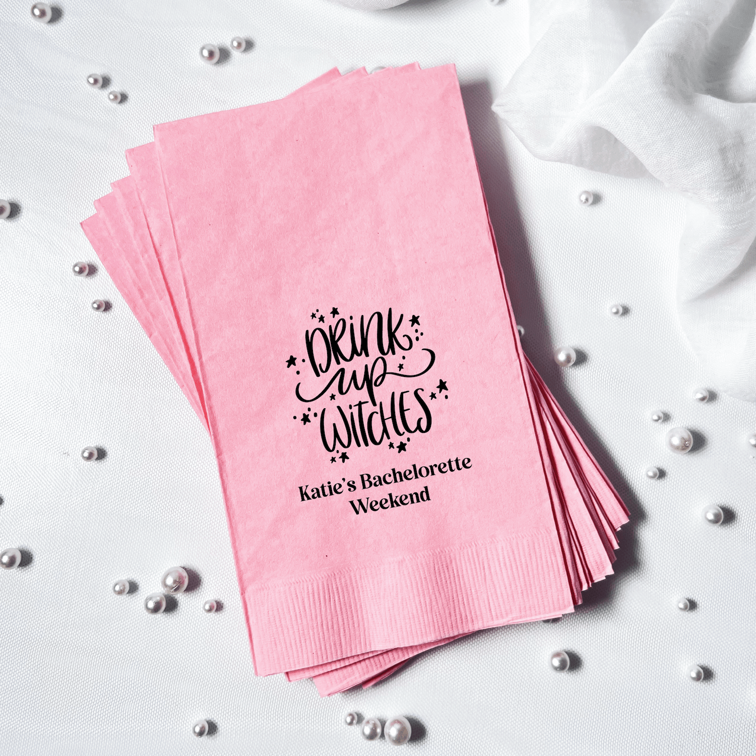 Stack of pink napkins with "Drink Up Witches" text and personalized "Katie's Bachelorette Weekend" message in black foil stamping