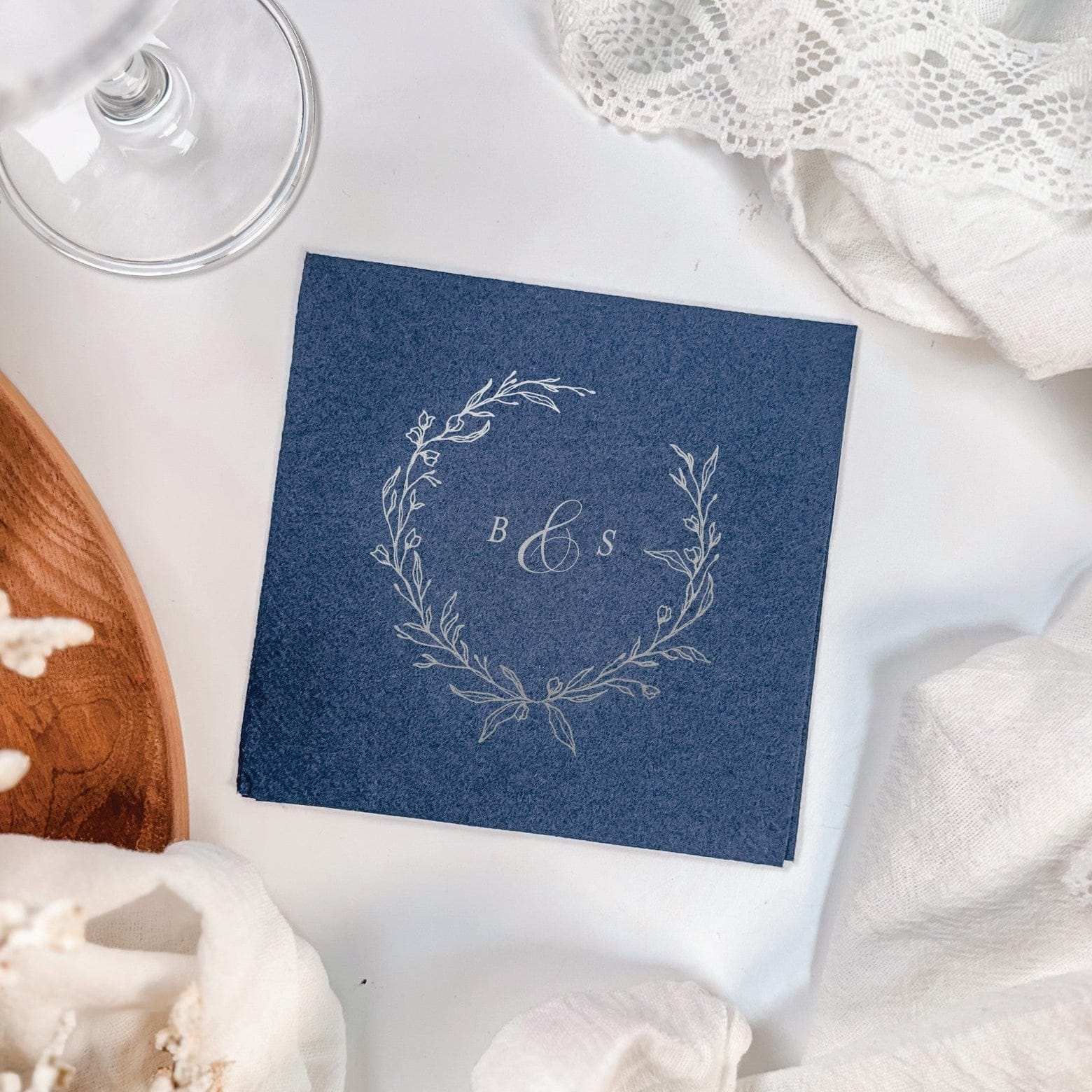A navy blue paper wedding napkin featuring a delicate silver foil botanical wreath design, perfect for elegant event decor.