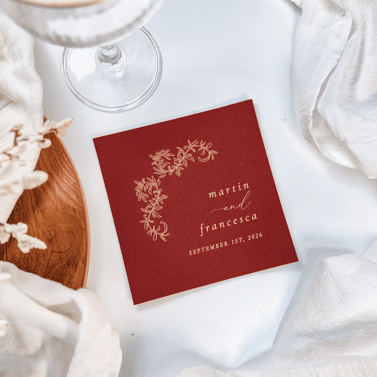 Deep red cocktail napkin with gold floral crest design and personalized names Martin and Francesca with wedding date September 27, 2024