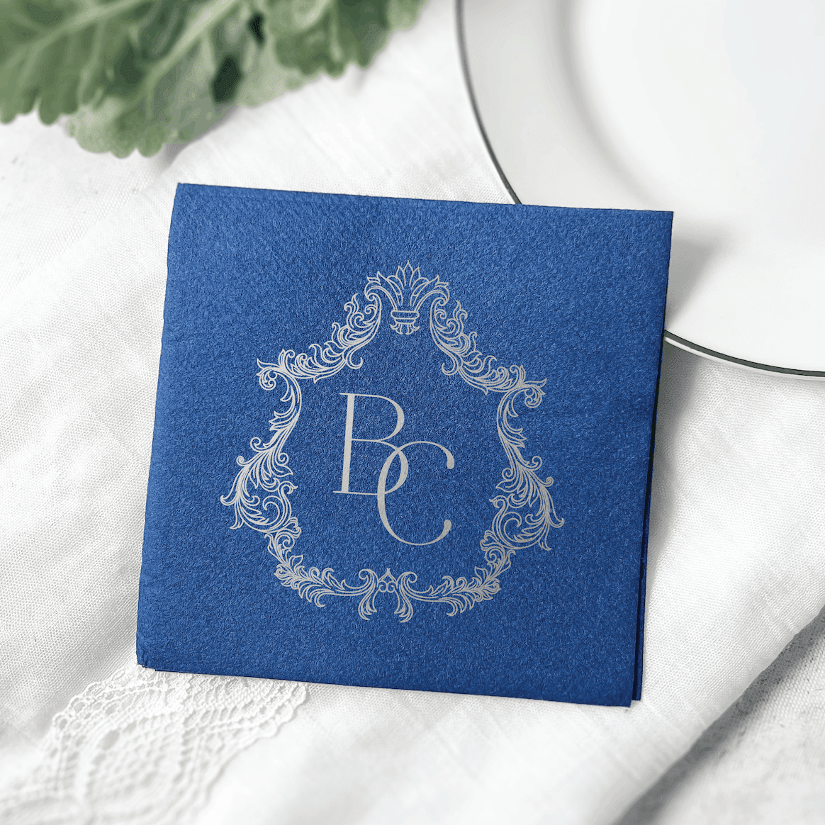Royal blue napkin with silver ornate frame monogram "BC" design and decorative scrollwork border