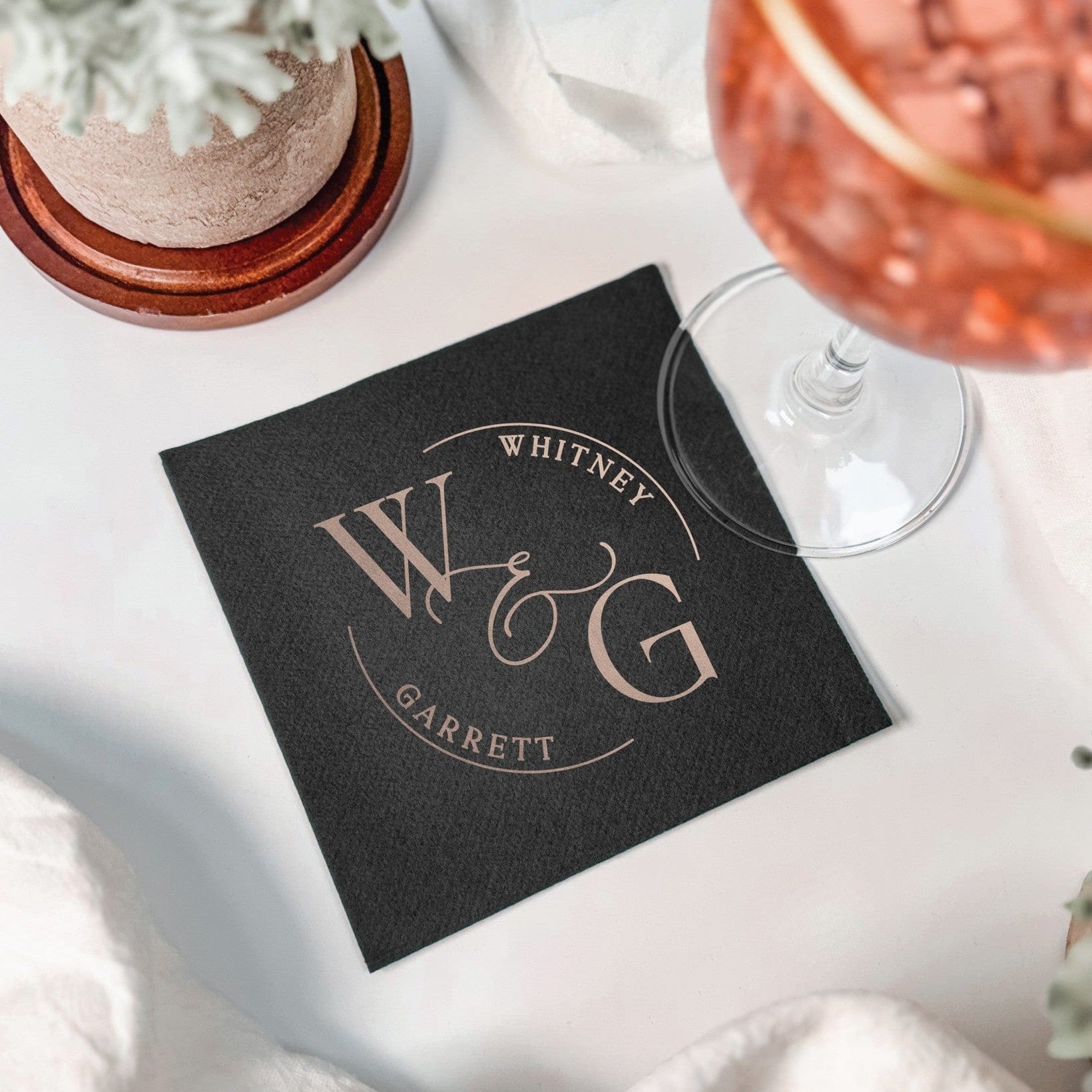 A black paper cocktail napkin featuring a metallic foil custom circular design, perfect for a wedding reception or elegant event.