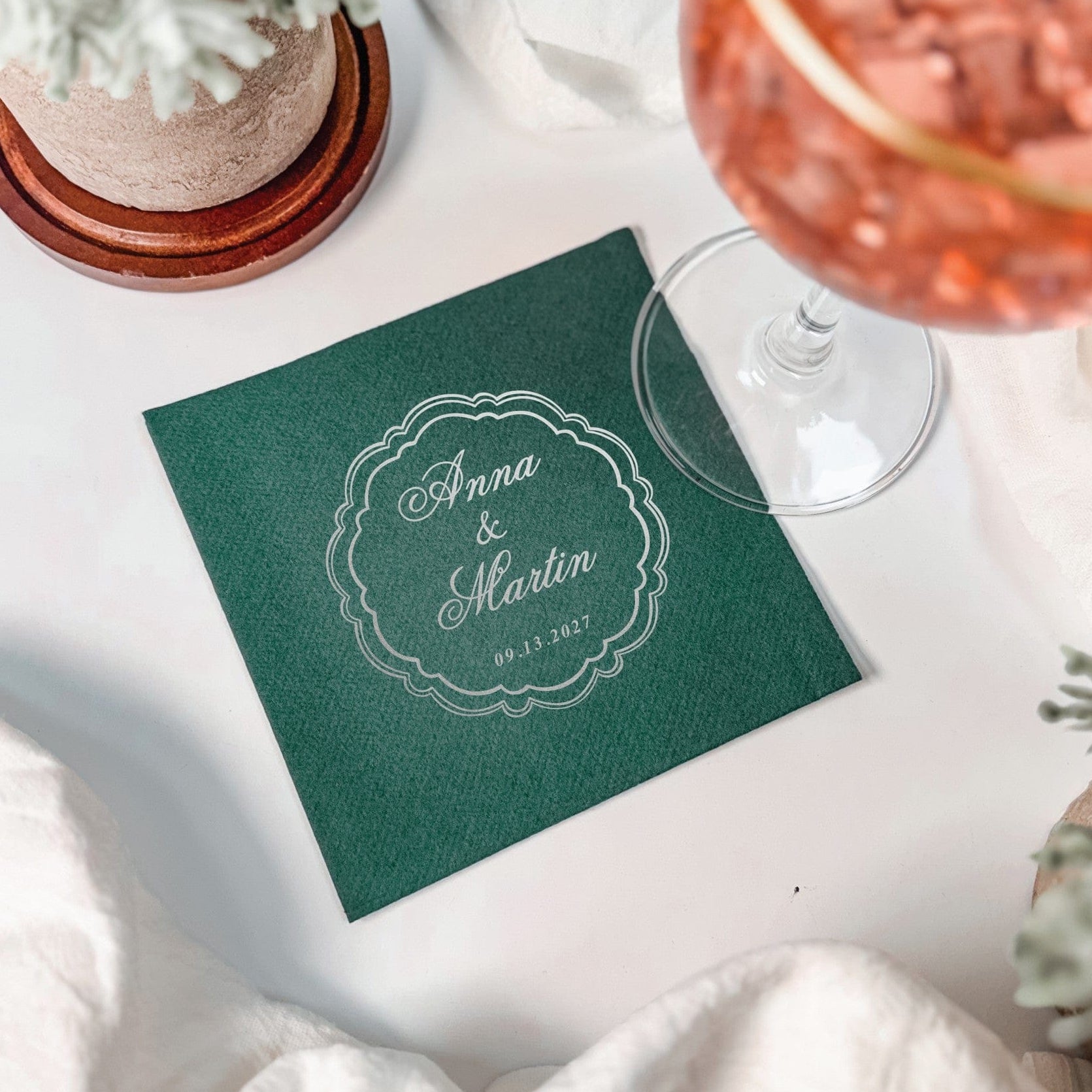 A dark green square personalized napkin features a silver foil scalloped oval design, perfect as wedding or event decor.