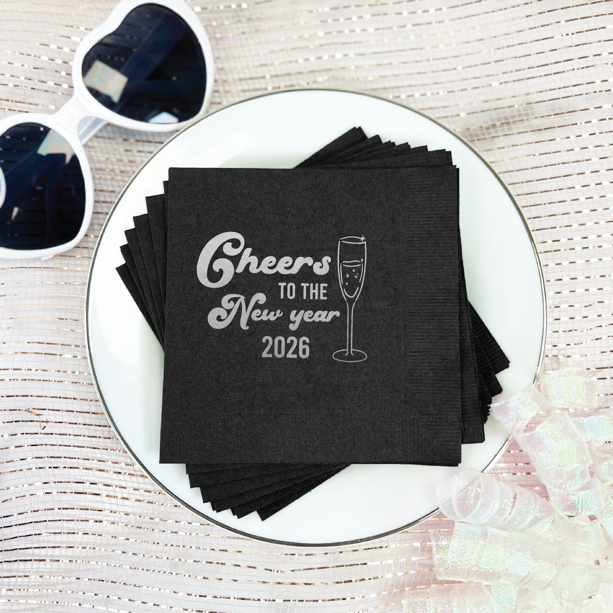 A stack of black paper beverage napkins, customized with a metallic silver design of a champagne flute, perfect for a festive occasion.