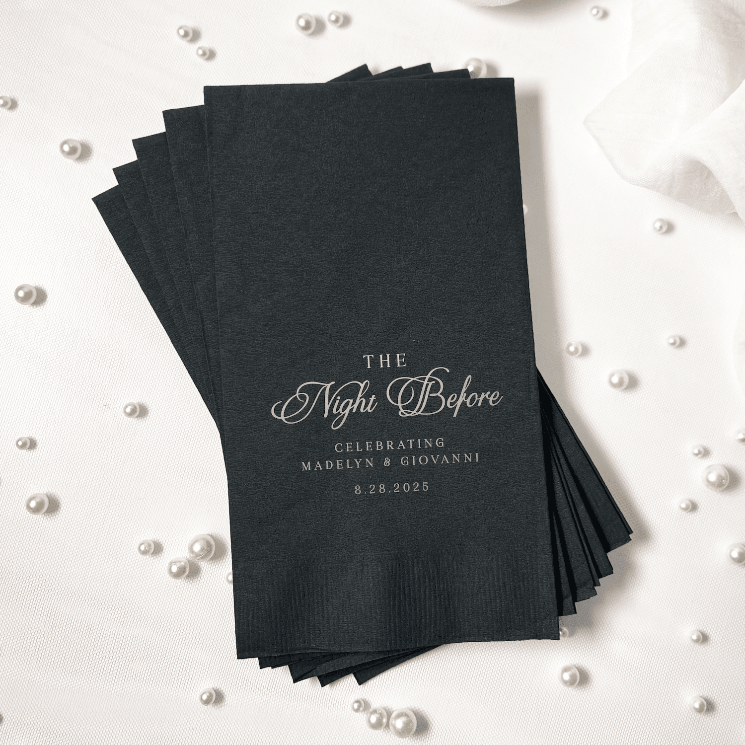 Stack of black foil-stamped napkins with "The Night Before" script text and wedding couple names and date personalization.