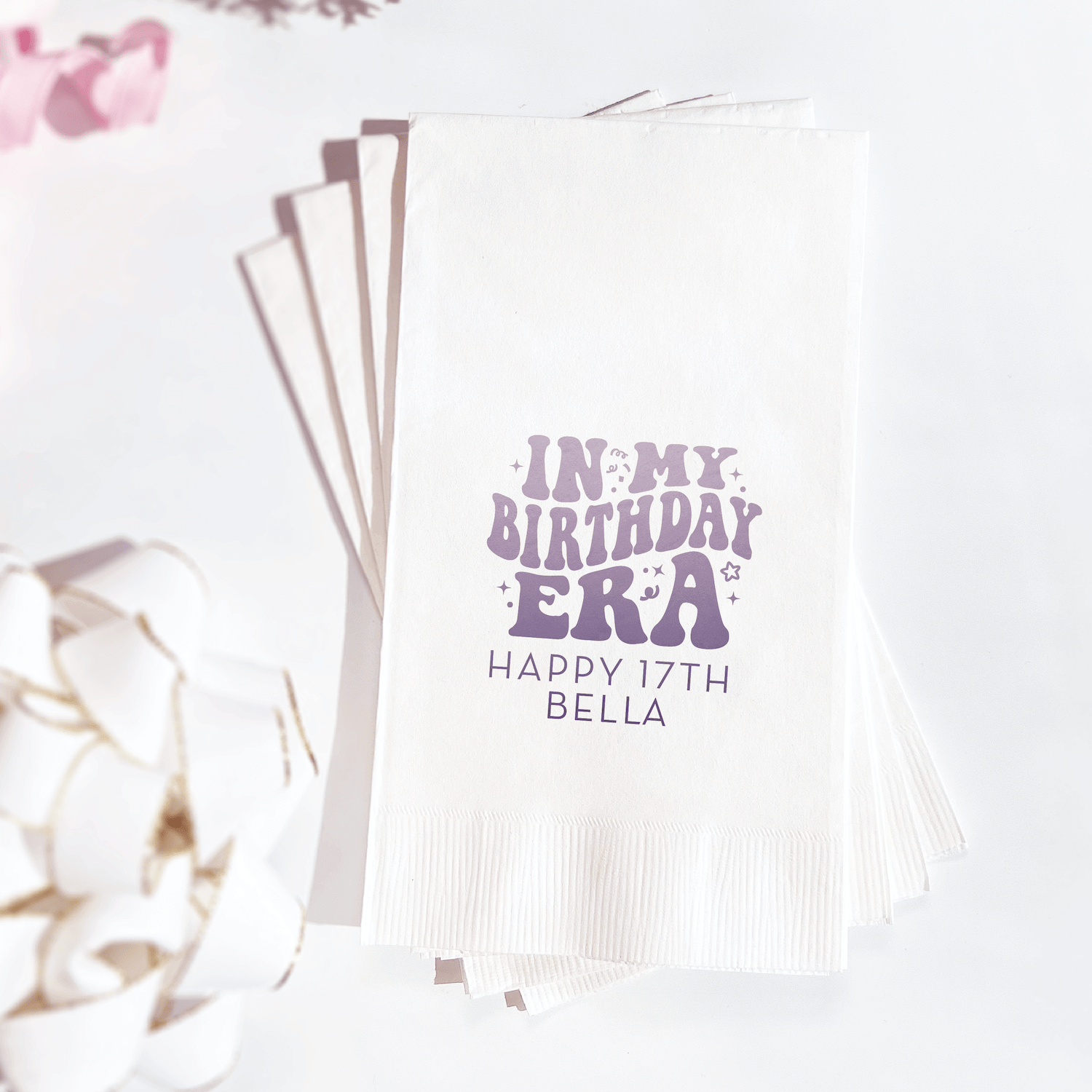 Stack of white napkins with purple foil-stamped text reading "In my birthday era" and "Happy 17th Bella" personalization.