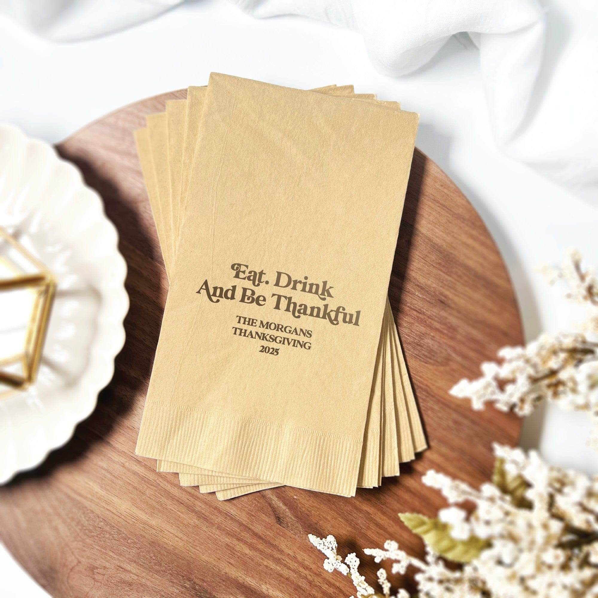 A stack of light brown folded paper guest towels, featuring a dark brown custom design, ideal for a Thanksgiving or fall-themed celebration.