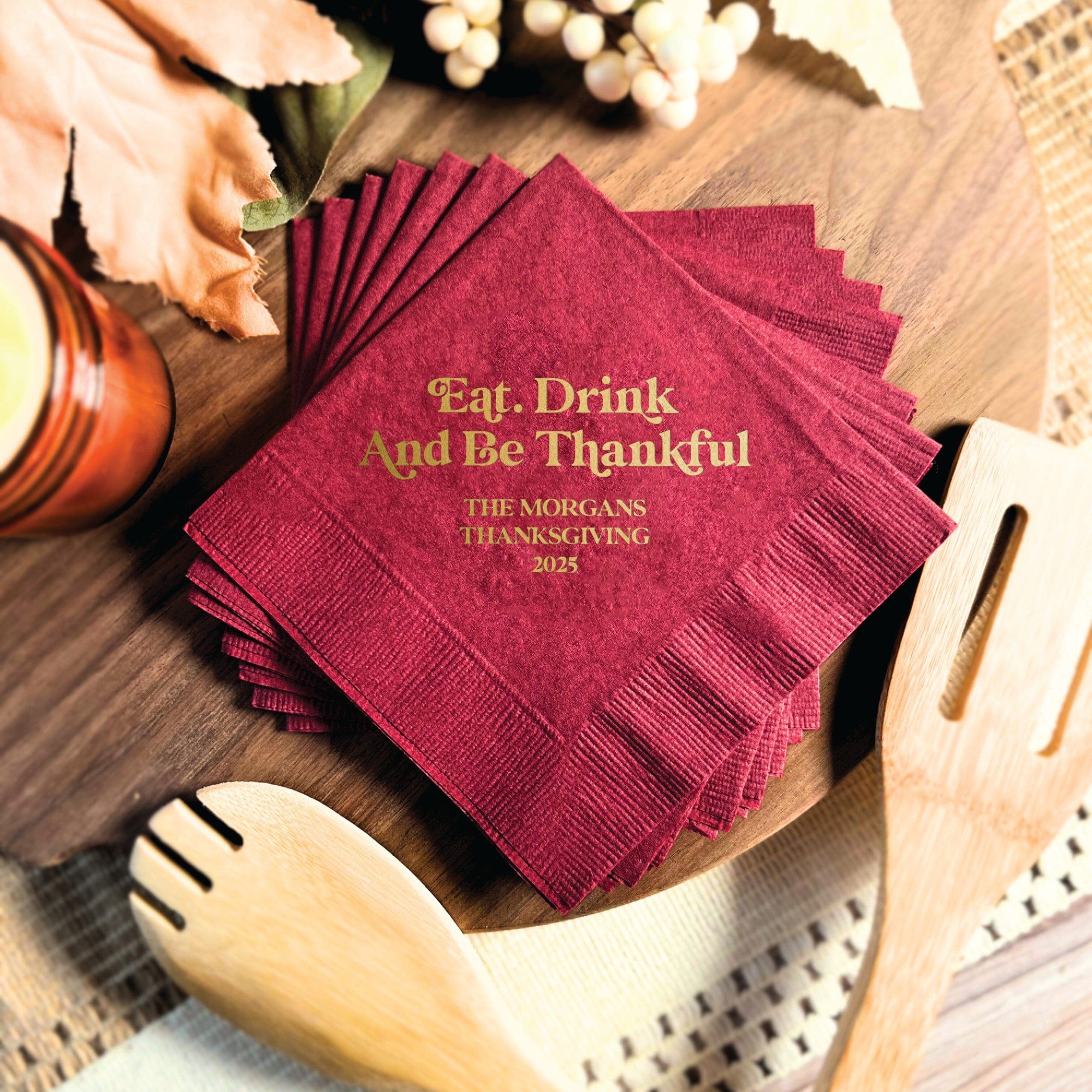 A stack of dark red paper napkins featuring gold foil printing, ideal for a festive fall event or Thanksgiving celebration.