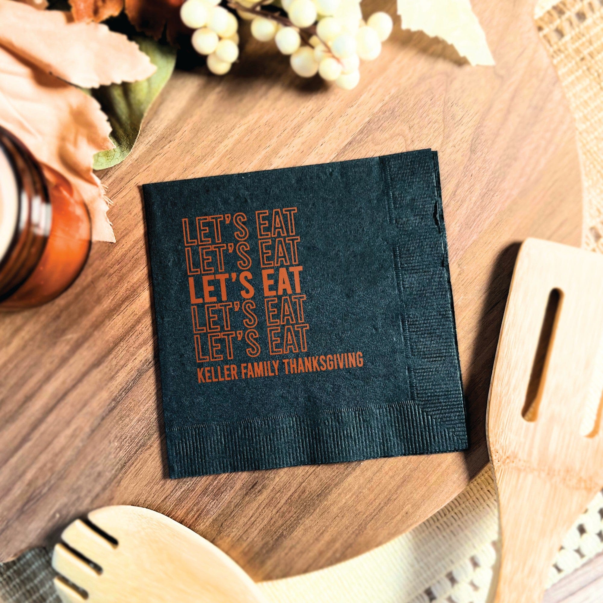 A dark gray folded disposable paper napkin with custom orange text, suitable for festive gatherings and personalized event decor.
