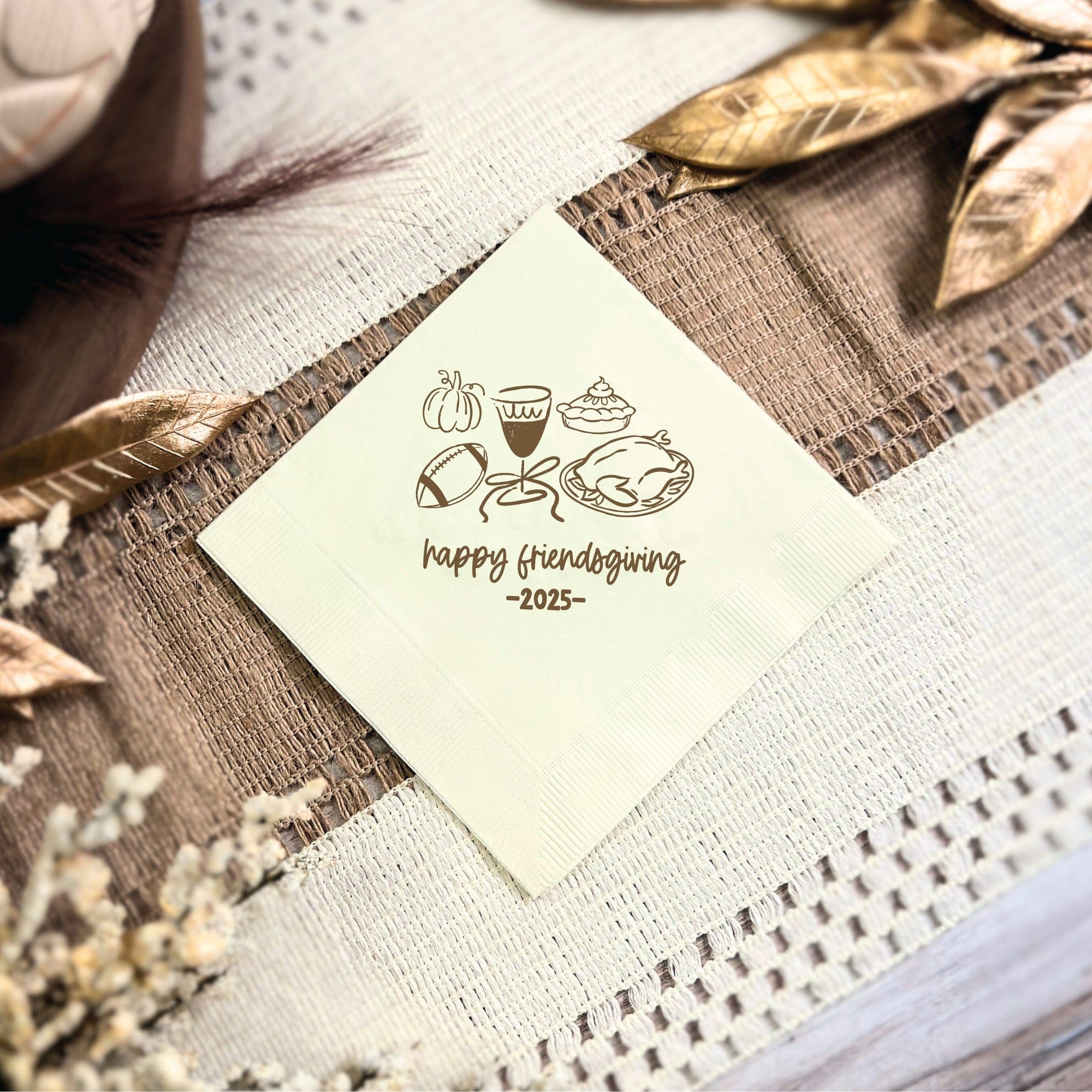 A personalized creamy white paper beverage napkin, featuring line art illustrations of fall and Friendsgiving themed items such as a pumpkin, pie, turkey, football, and a drink, suitable for a fall celebration.