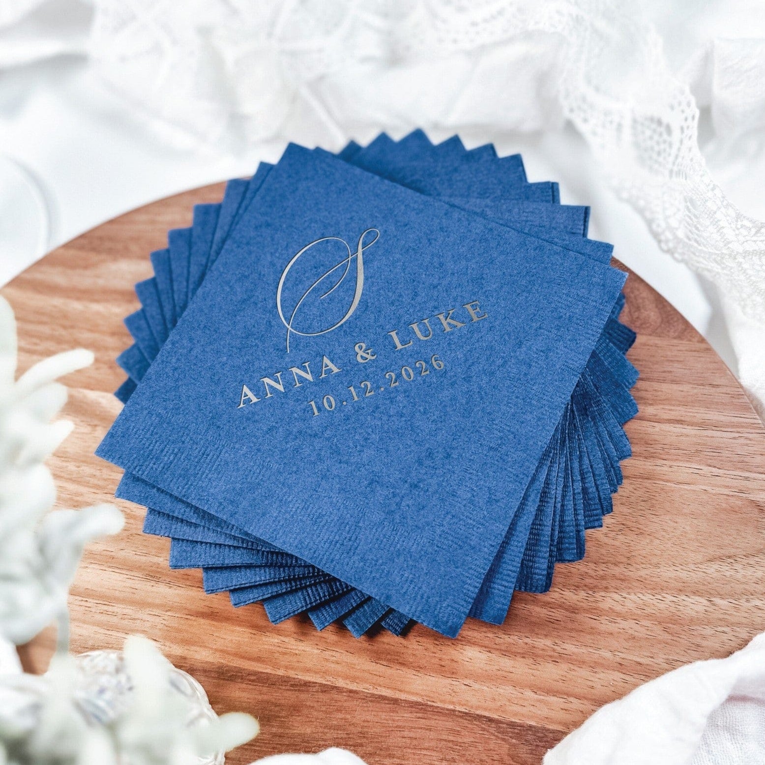 A stack of blue paper wedding napkins features a personalized gold foil design, perfect for elegant event decor.