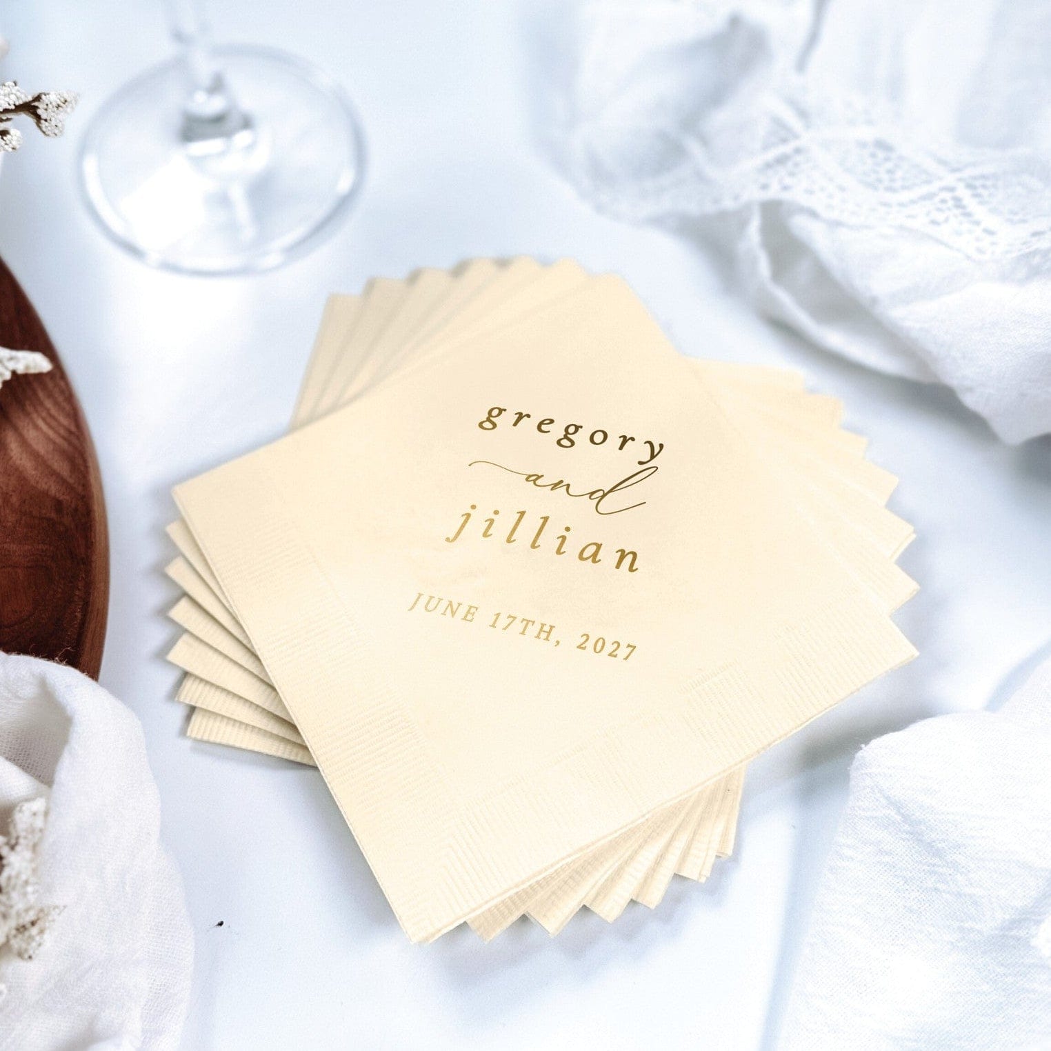 A stack of light cream paper wedding napkins features a custom gold foil print, ideal for personalized event decor.