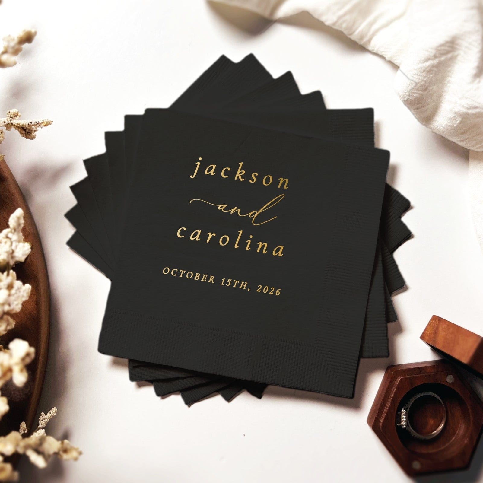 A stack of black paper wedding napkins featuring elegant gold foil script, suitable for a personalized event.
