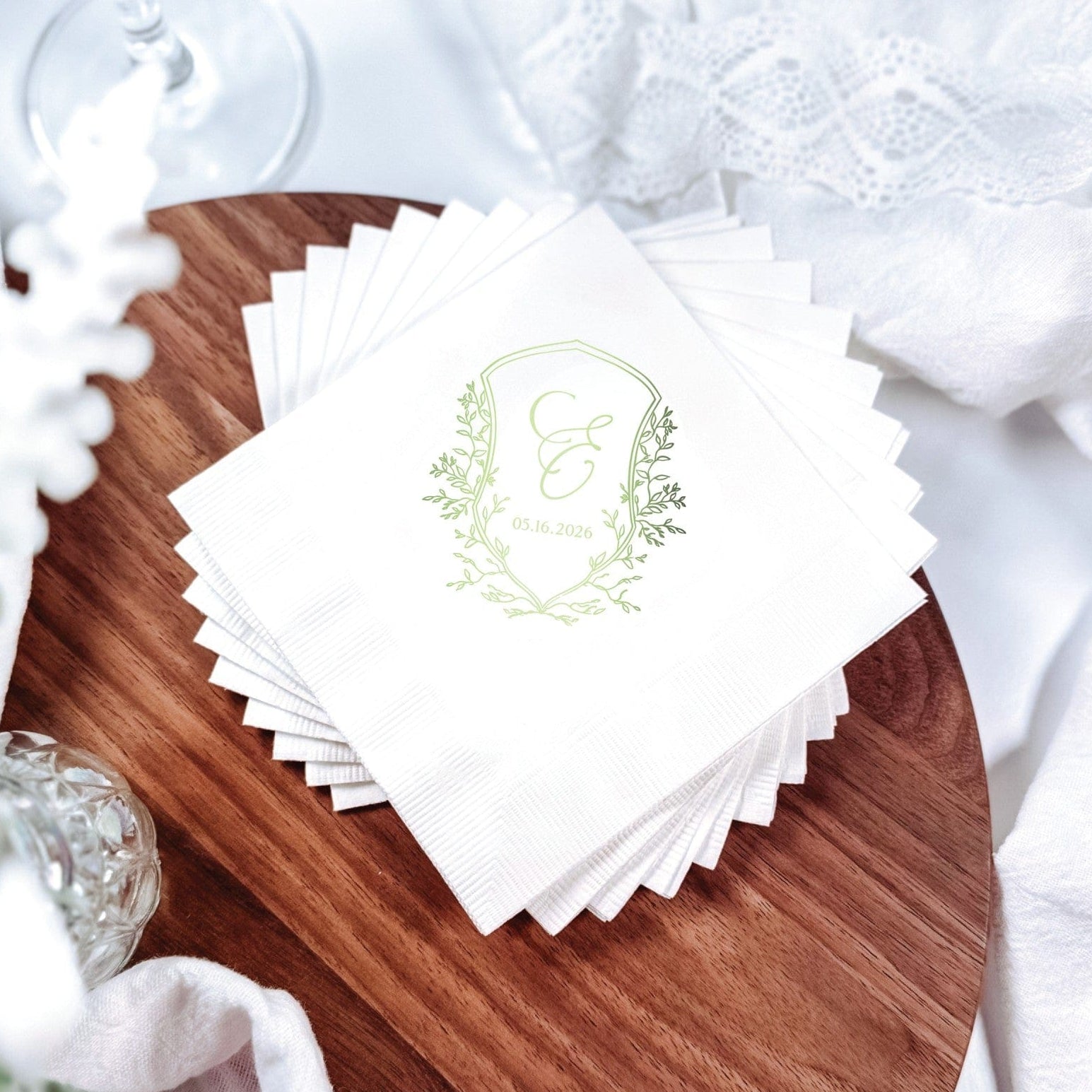 A stack of white paper wedding napkins, personalized with a green leaf crest design, perfect for a reception.