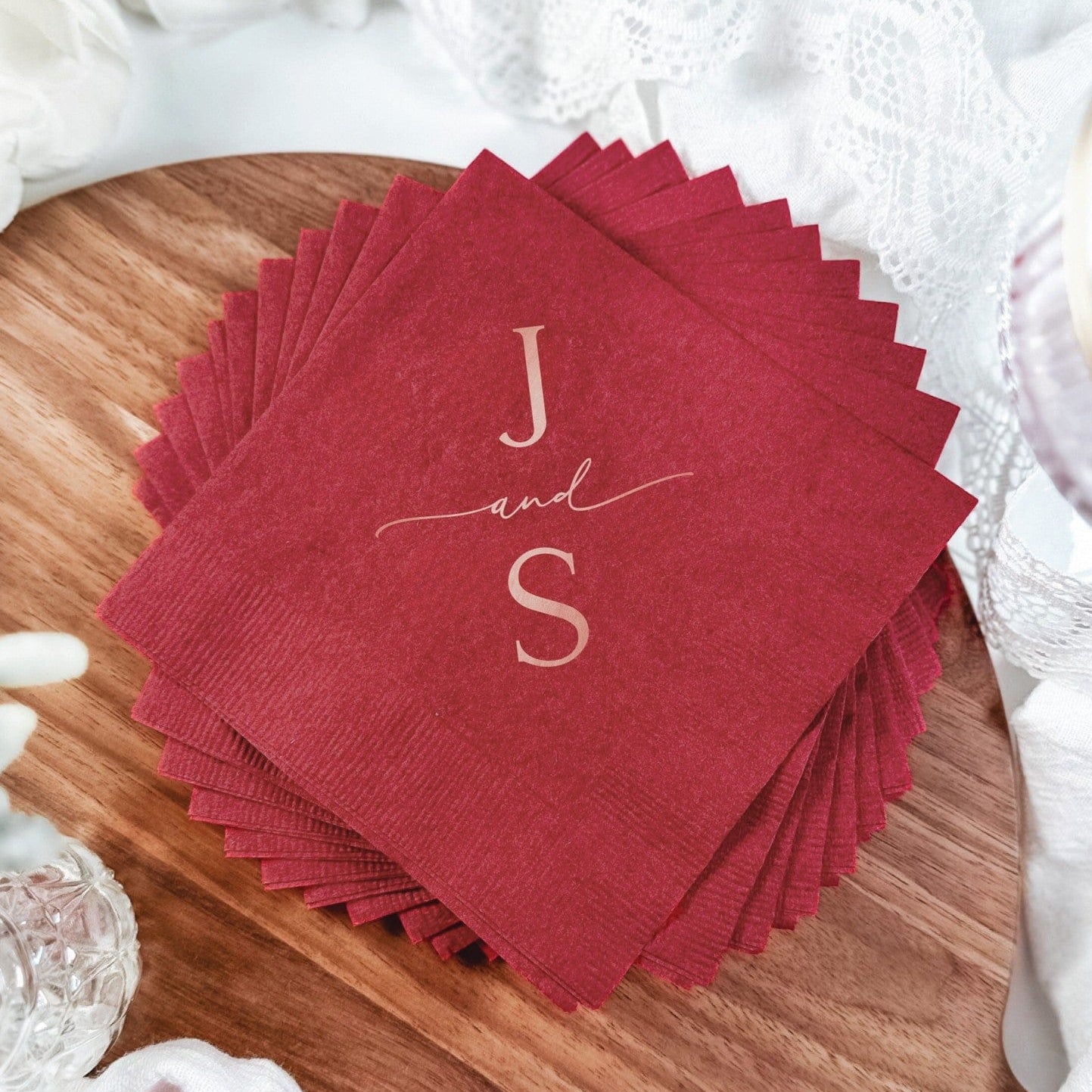 A stack of deep red paper napkins featuring a custom metallic foil initial design, perfect for a wedding or elegant event.
