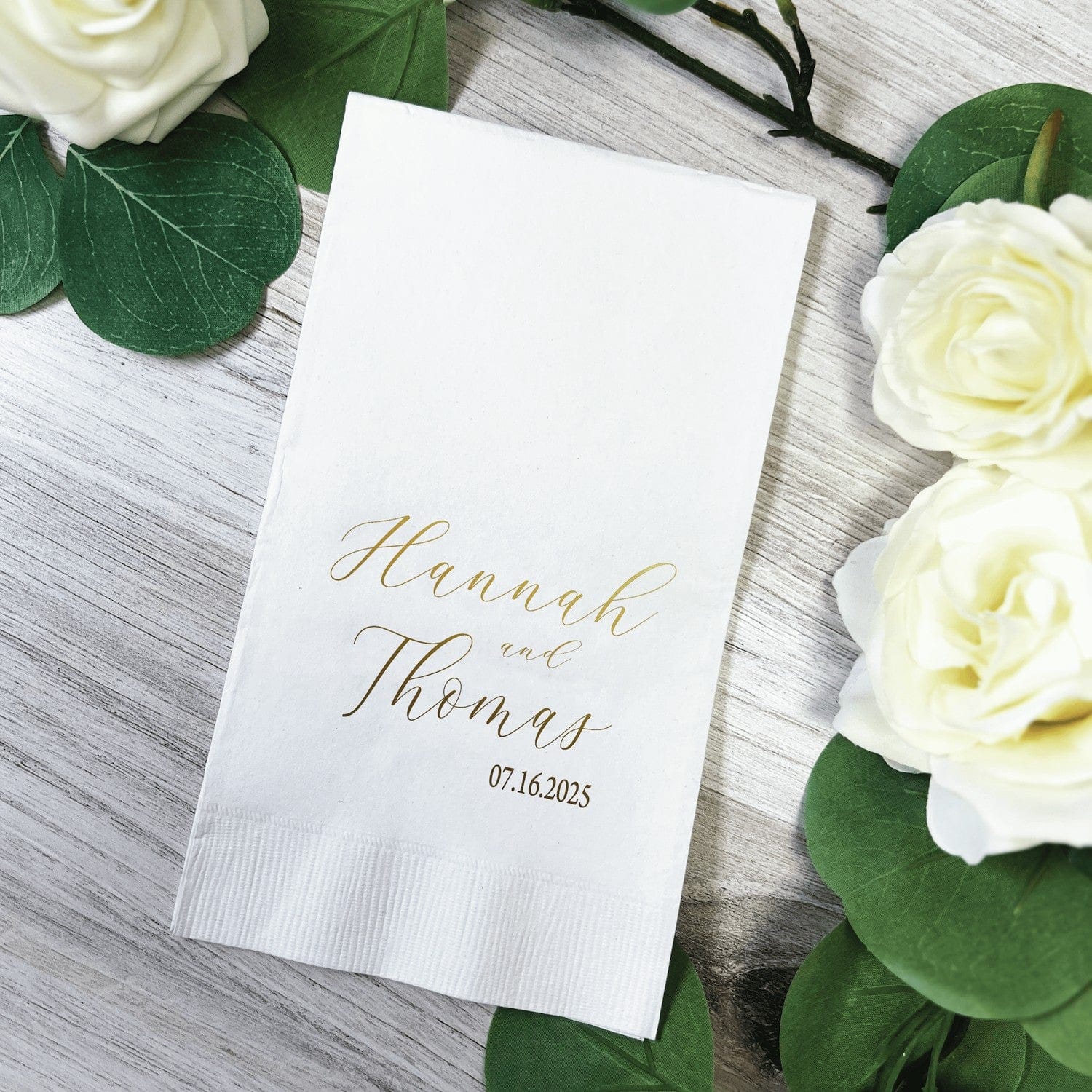 A white paper guest towel featuring elegant gold foil script print, ideal for wedding or event receptions.