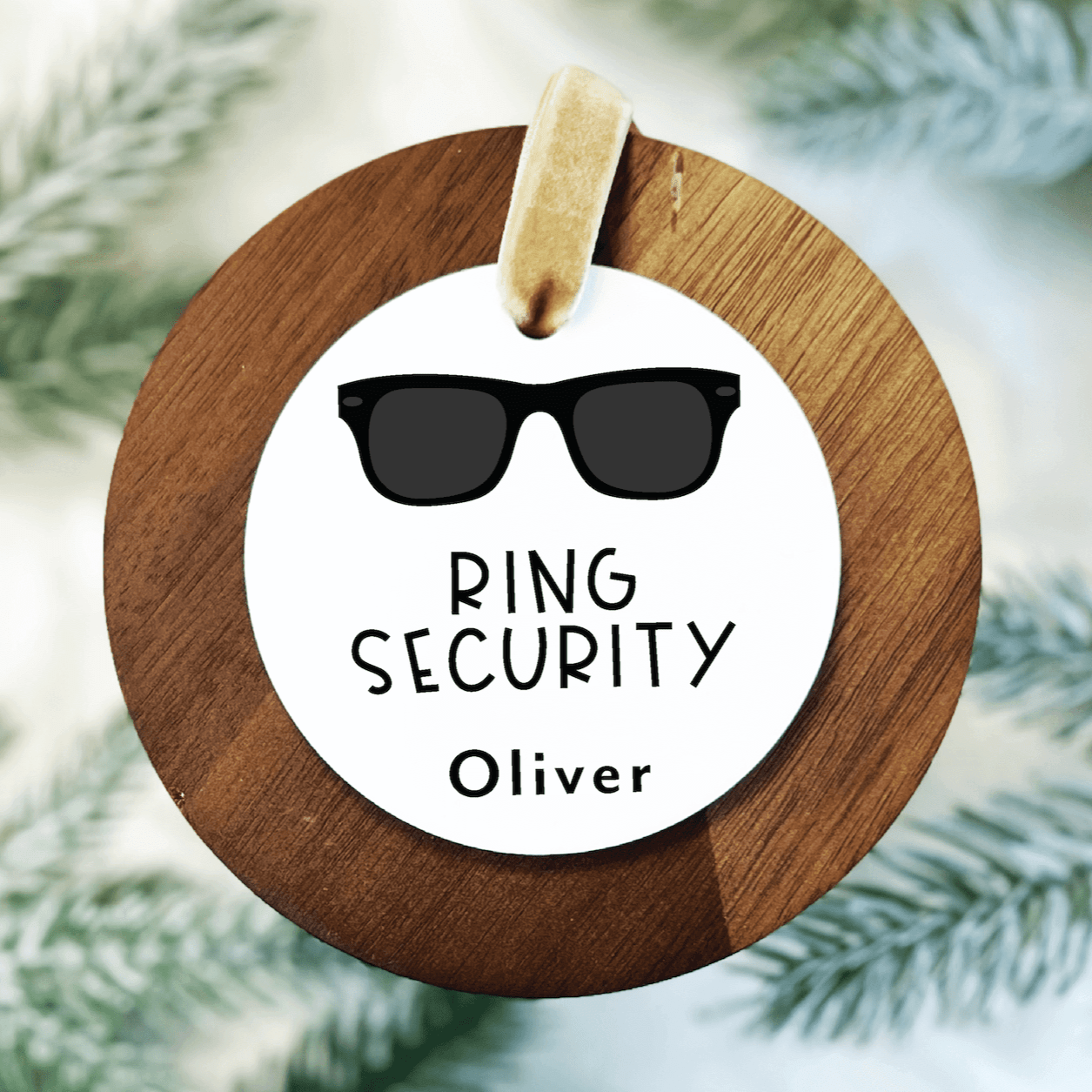 White acrylic ornament with sunglasses illustration, "RING SECURITY" text, and personalized name "Oliver" on wooden ring hanger with twine.
