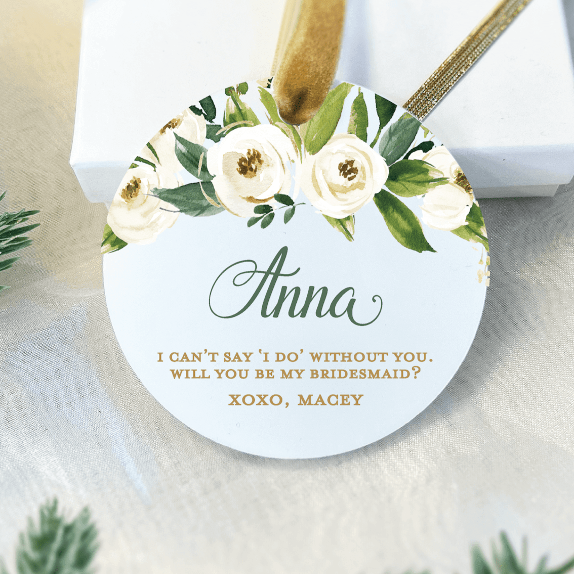 White acrylic ornament with white and gold flowers, personalized name "Anna" and bridesmaid proposal message with gold text and twine hanger.