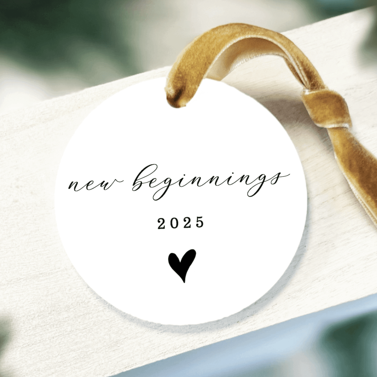 White acrylic ornament with gold ribbon featuring "new beginnings 2025" text and heart design.
