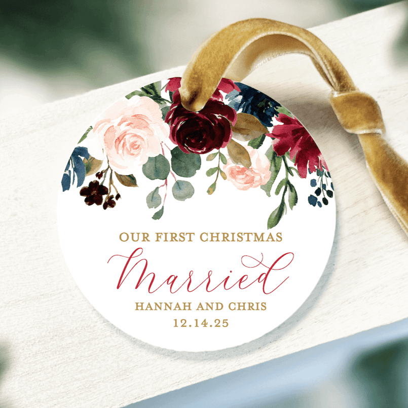 White acrylic ornament with burgundy and blush florals, gold text reading "Our First Christmas Married" and personalized names with date, tied with tan ribbon.