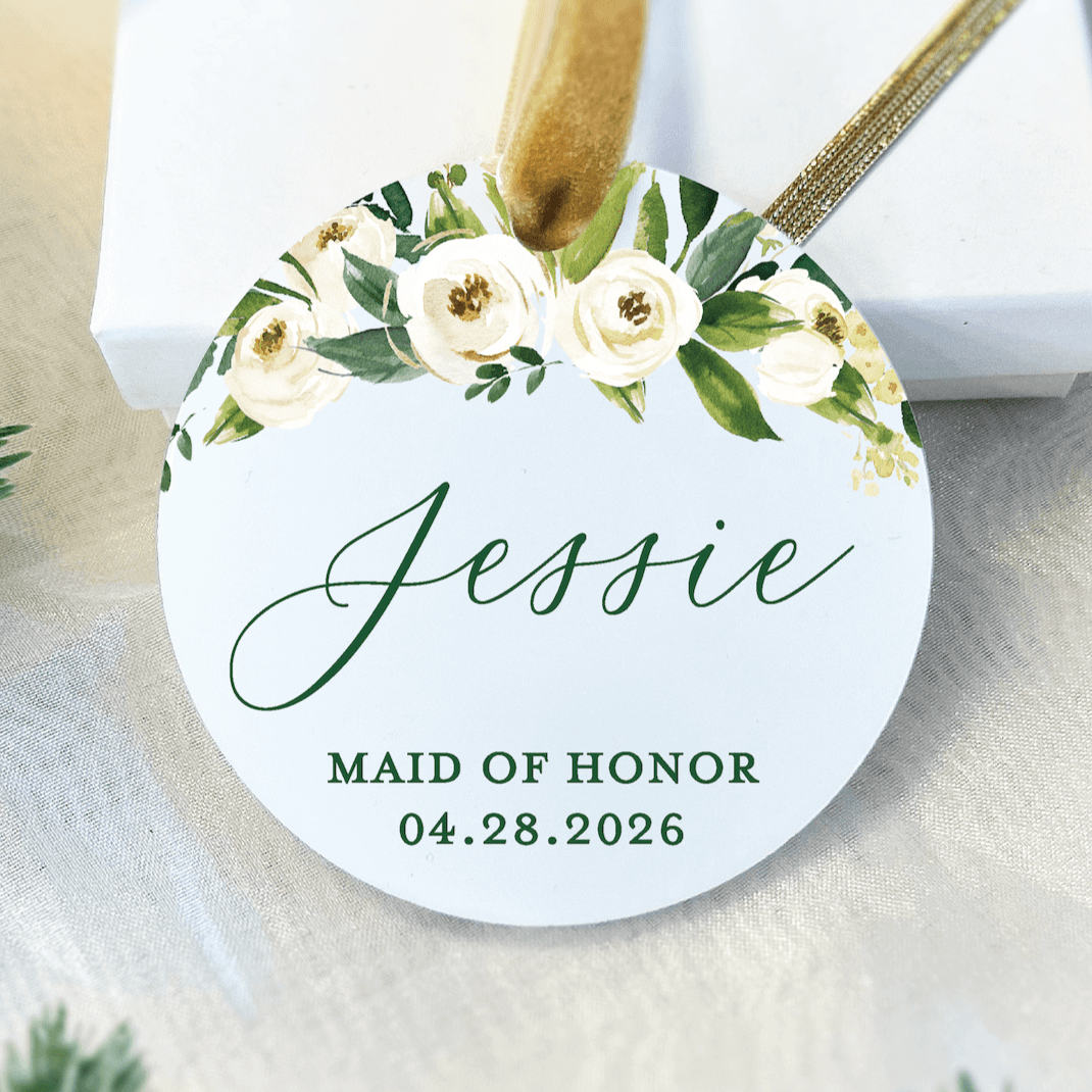 White acrylic ornament with cream floral design, personalized name "Jessie" and "MAID OF HONOR 04.28.2026" text