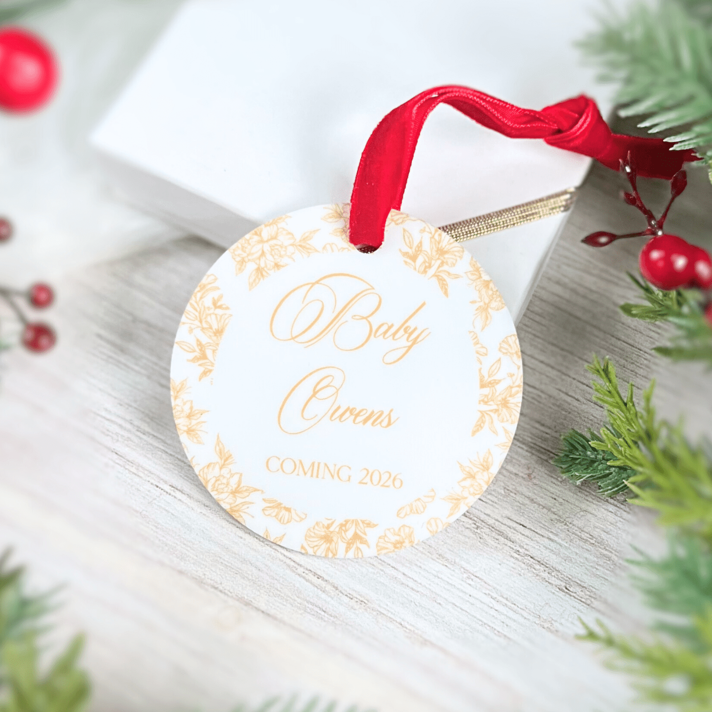 Round acrylic ornament with gold toile border, red ribbon, personalized with "Baby Owens Coming 2020" in gold script text