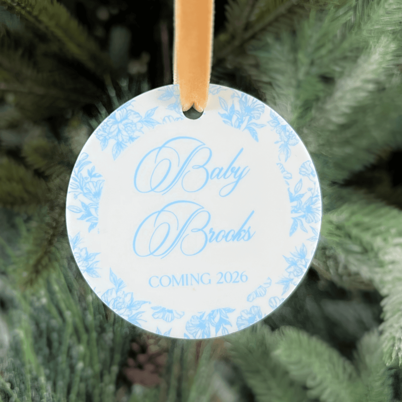 Round acrylic ornament with blue toile pattern border and gold ribbon, personalized with "Baby Brooks Coming 2026" text.