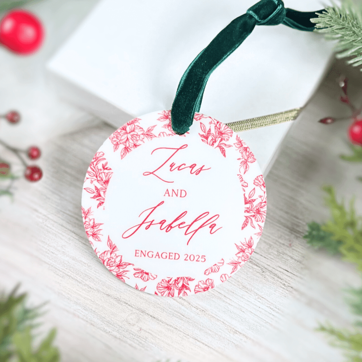 Round acrylic ornament with pink floral toile border featuring "Hers and His" script text and "Engaged 2025" with dark green ribbon loop.