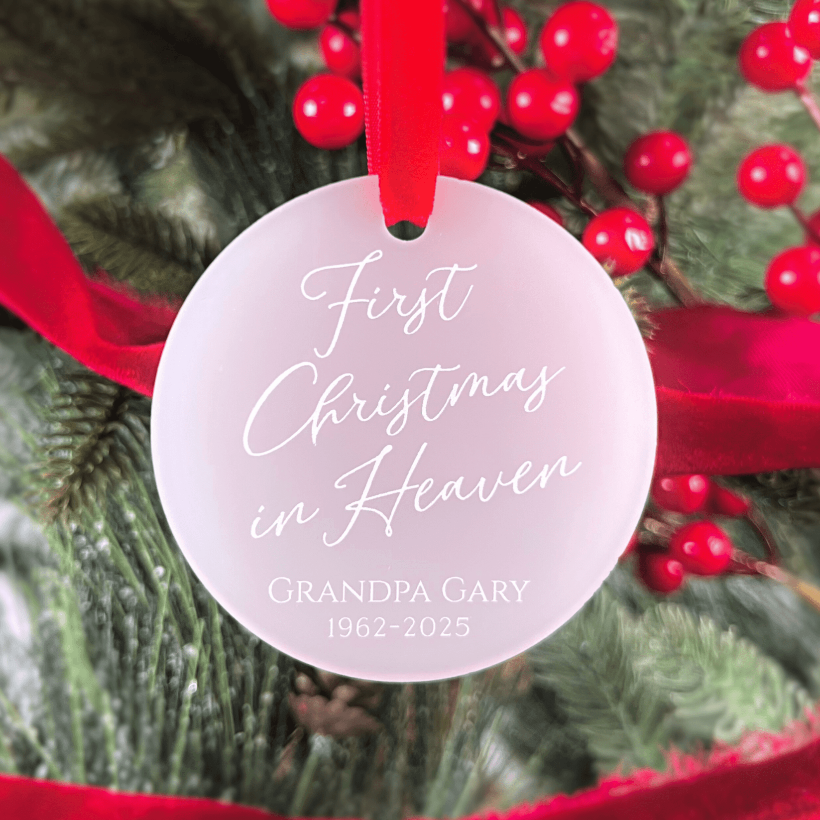 White acrylic round ornament with red ribbon featuring "First Christmas in Heaven" and "GRANDPA GARY 1962-2025" engraved in script text.