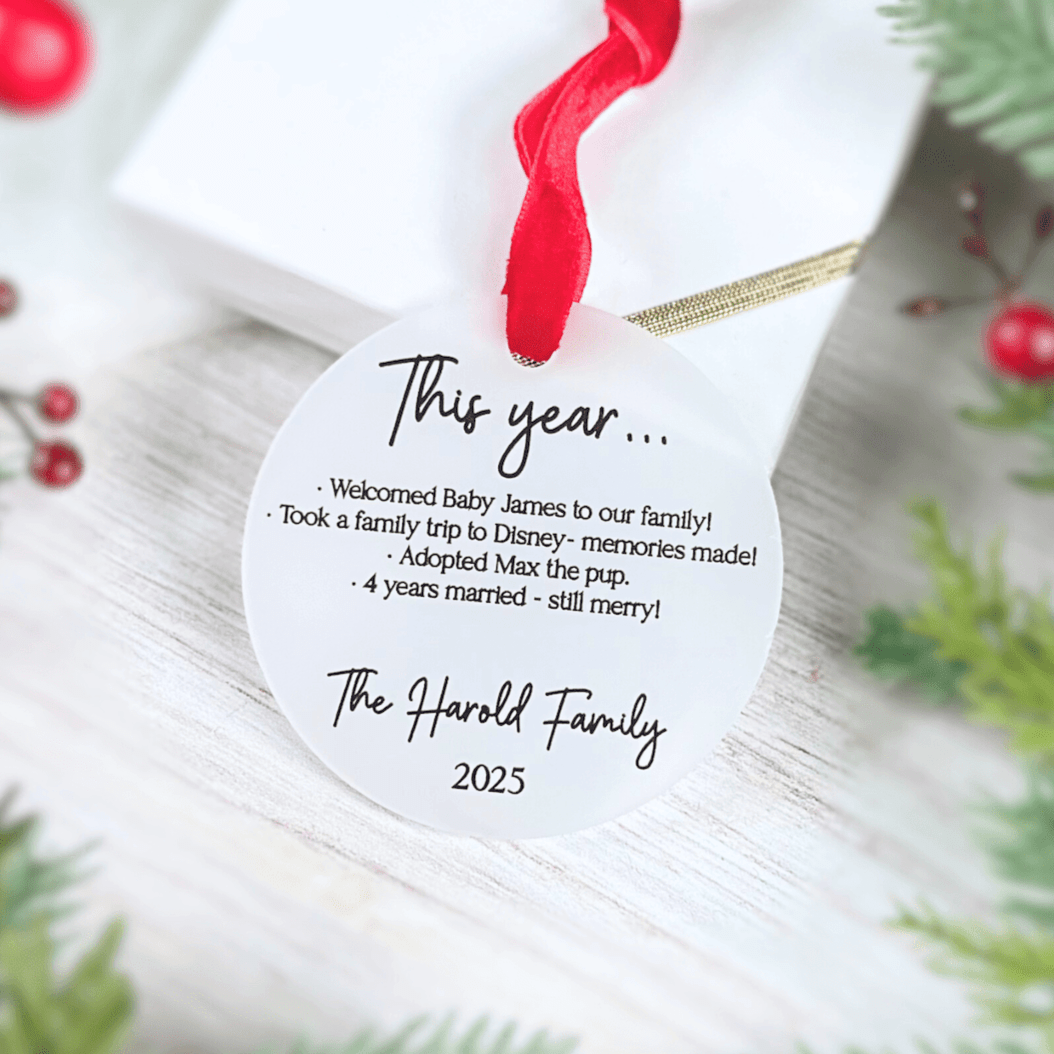 White acrylic ornament with red ribbon featuring "This year..." family highlights and "The Harold Family 2025" personalization text.