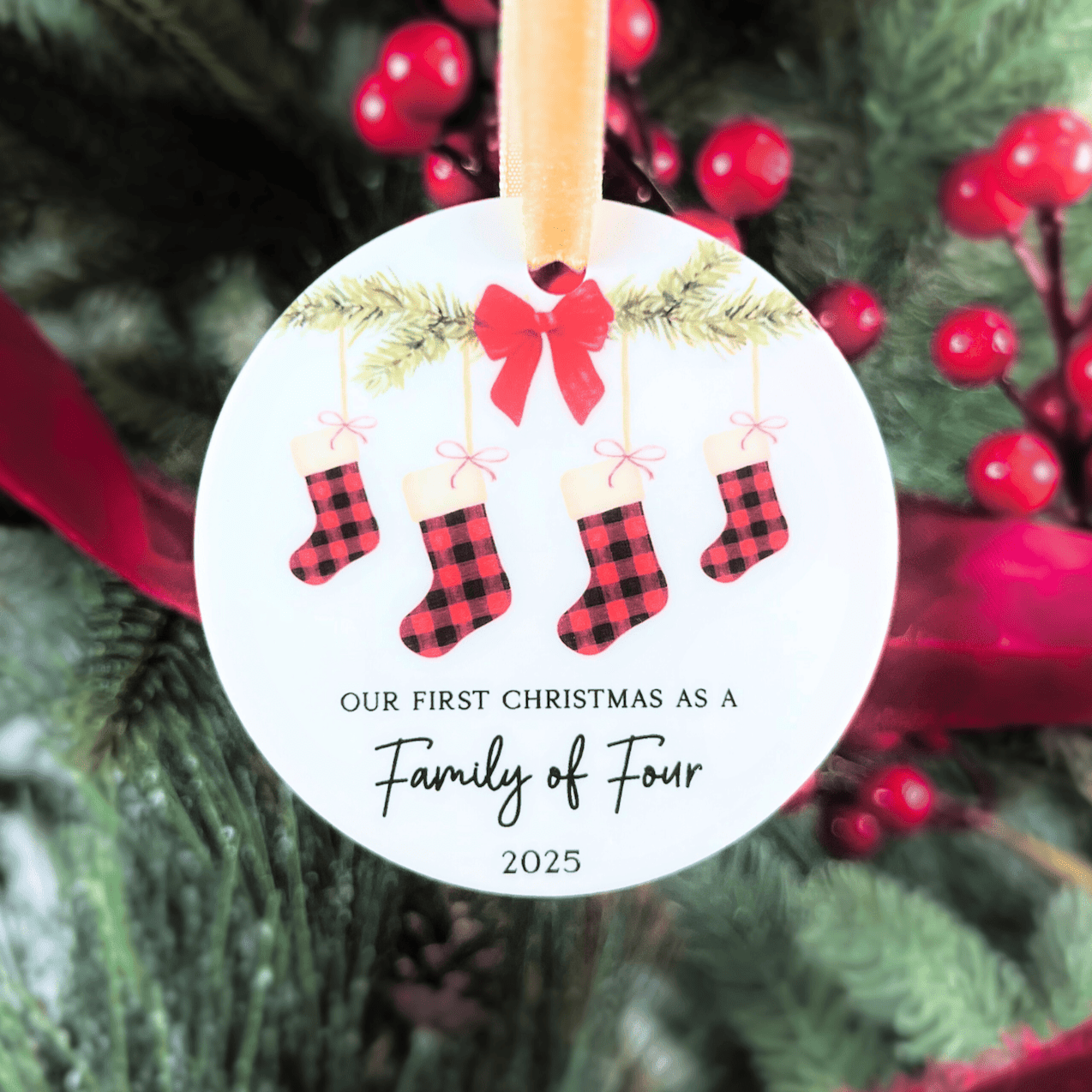 White acrylic ornament with red plaid stockings, bow, and text reading "Our First Christmas as a Family of Four 2025"