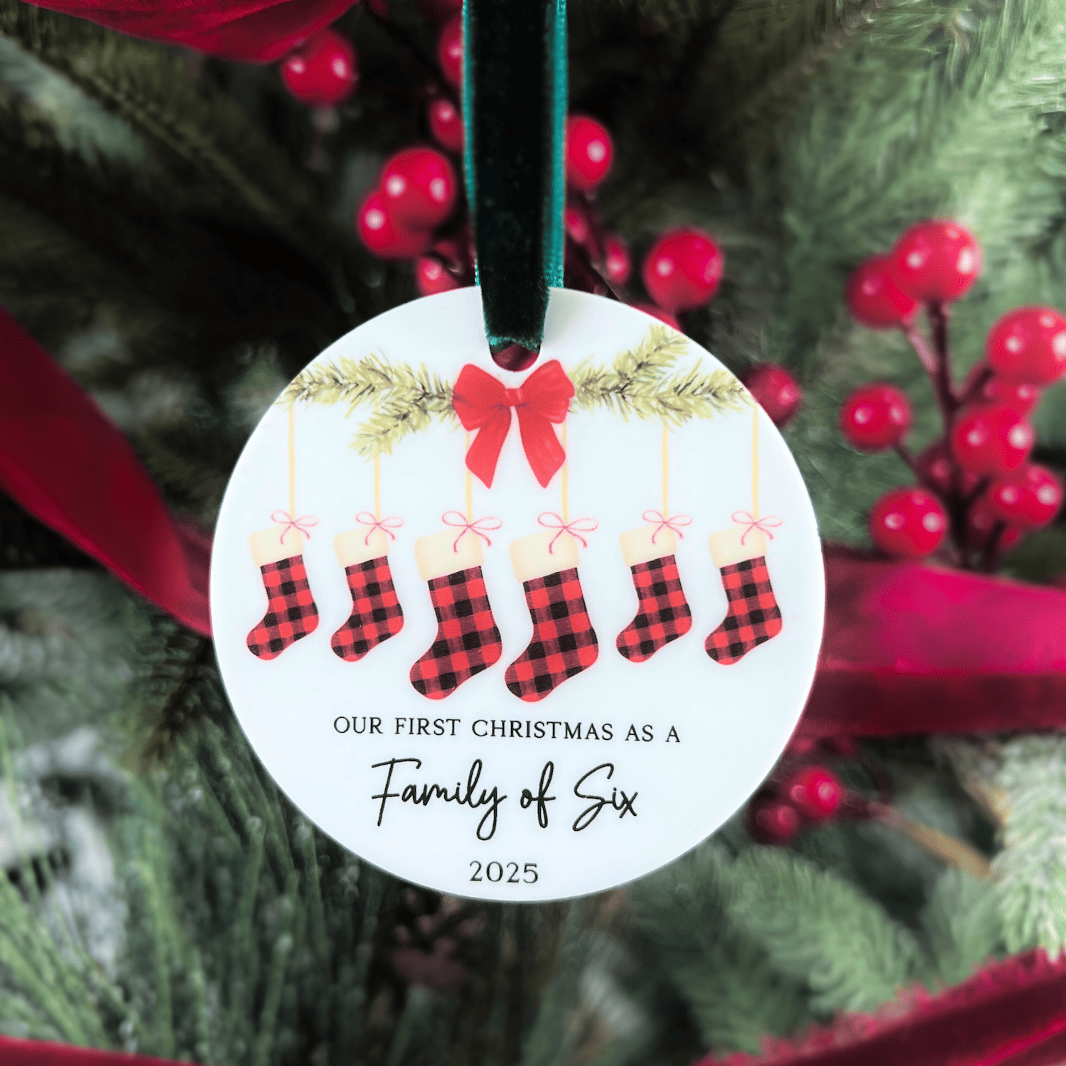 White round acrylic ornament with red plaid stockings, red bow, gold garland, and text reading "Our First Christmas as a Family of Six 2025"