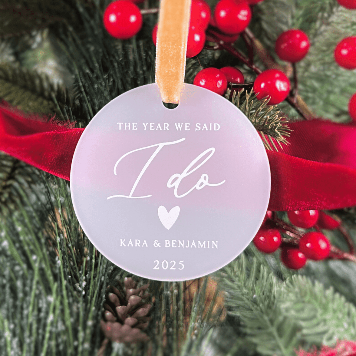 Lavender acrylic ornament with gold ribbon, personalized with "The Year We Said I Do," couple names, and 2025, displayed on festive evergreen garland with red berries.