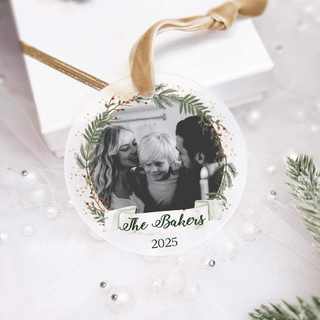 Round acrylic ornament with gold ribbon featuring black and white family photo surrounded by green wreath design and "The Bakers 2025" text.