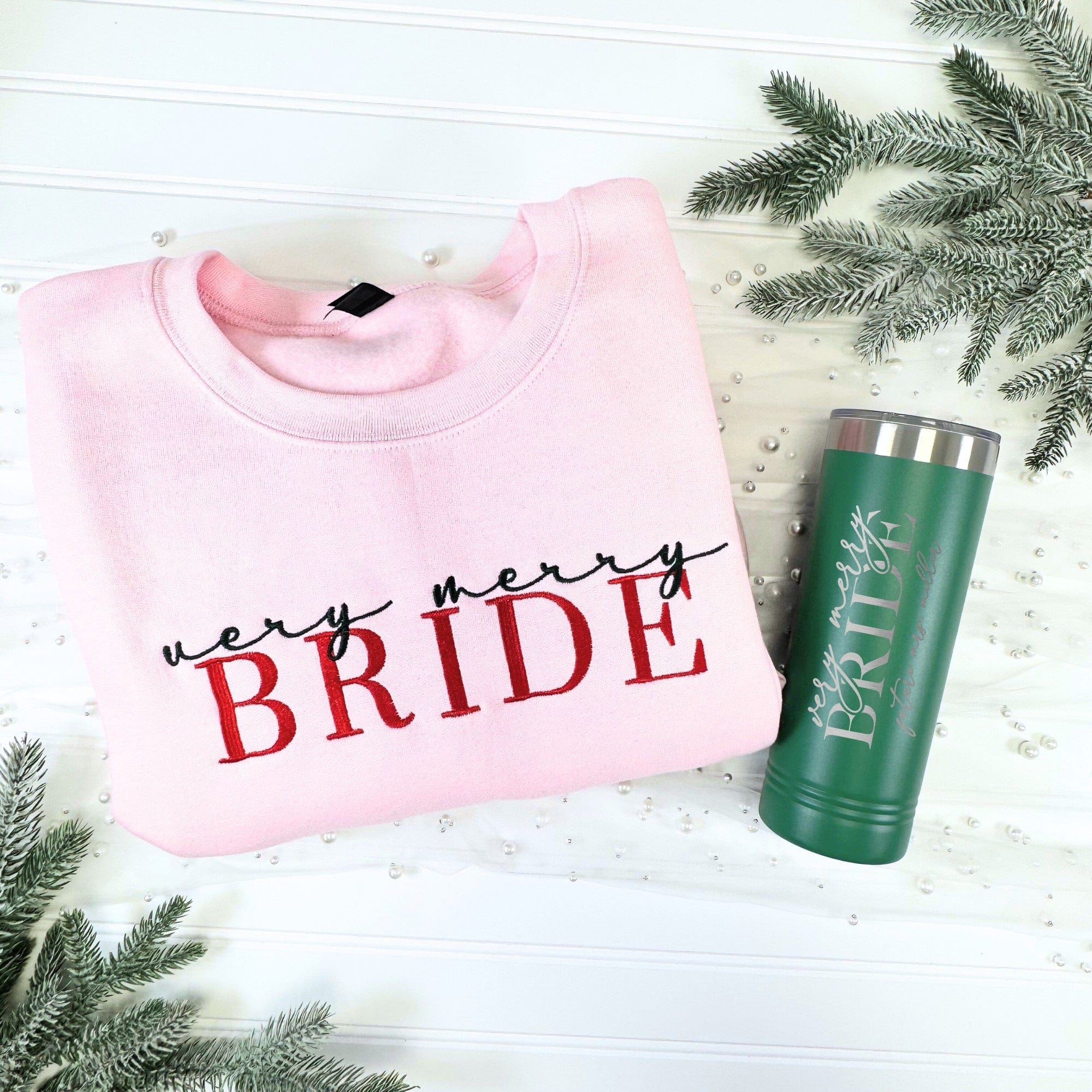 A light pink crewneck sweatshirt made of soft fabric paired with a dark green insulated metal tumbler, suitable for bridal celebrations.