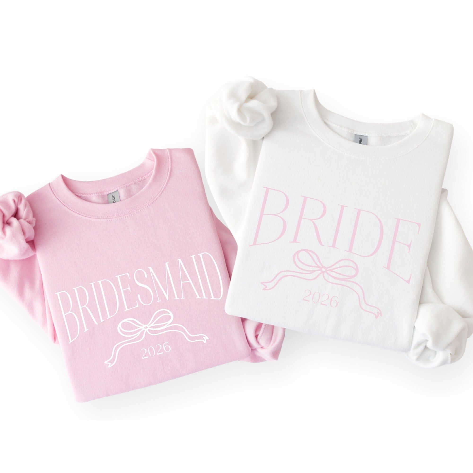 Two soft crewneck sweatshirts, one light pink and one white, featuring a delicate ribbon bow graphic, ideal for a bridal event.