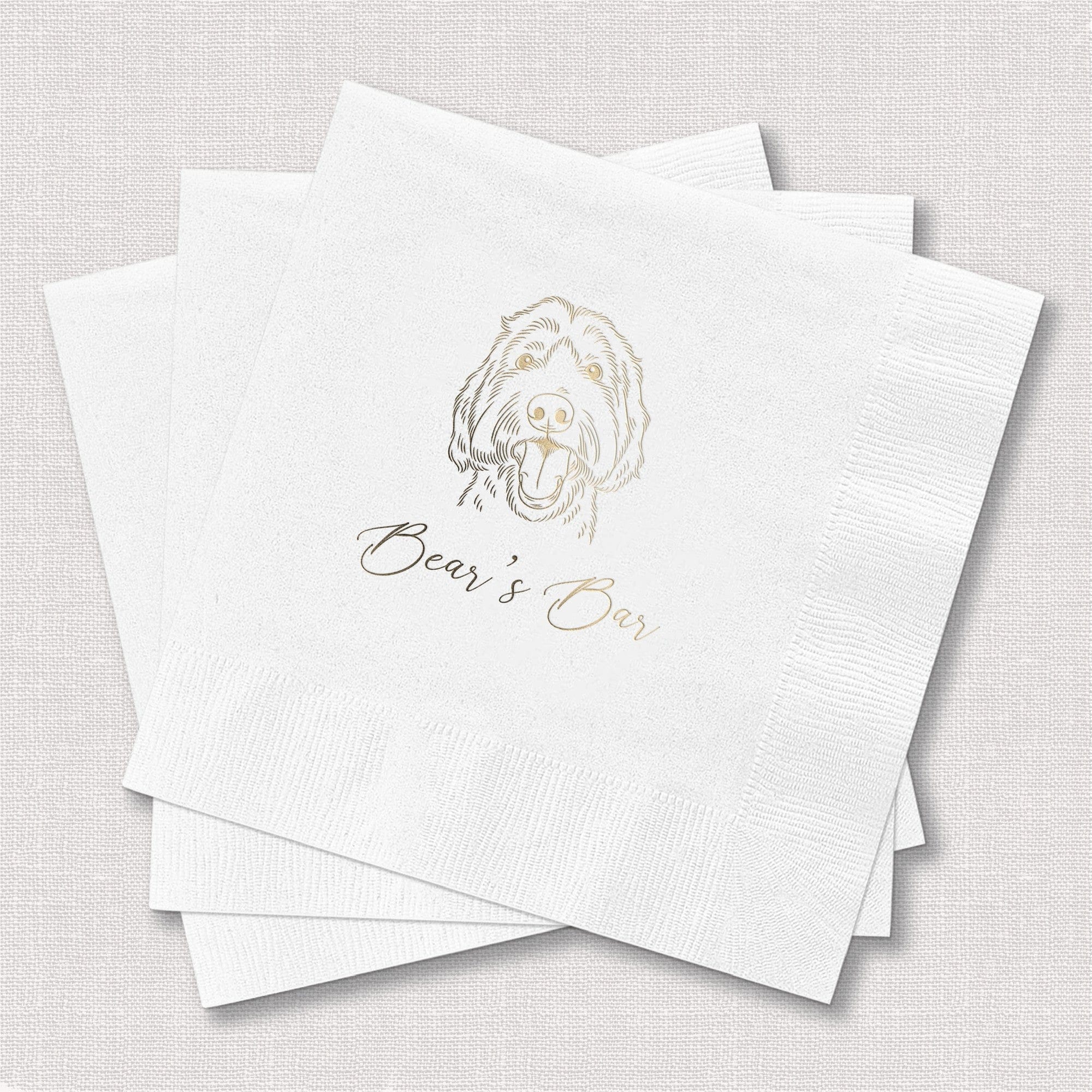 A stack of white textured cocktail napkins personalized with a gold foil-stamped illustration of a happy dog's head and elegant script, ideal for a wedding, bridal shower, or birthday celebration.