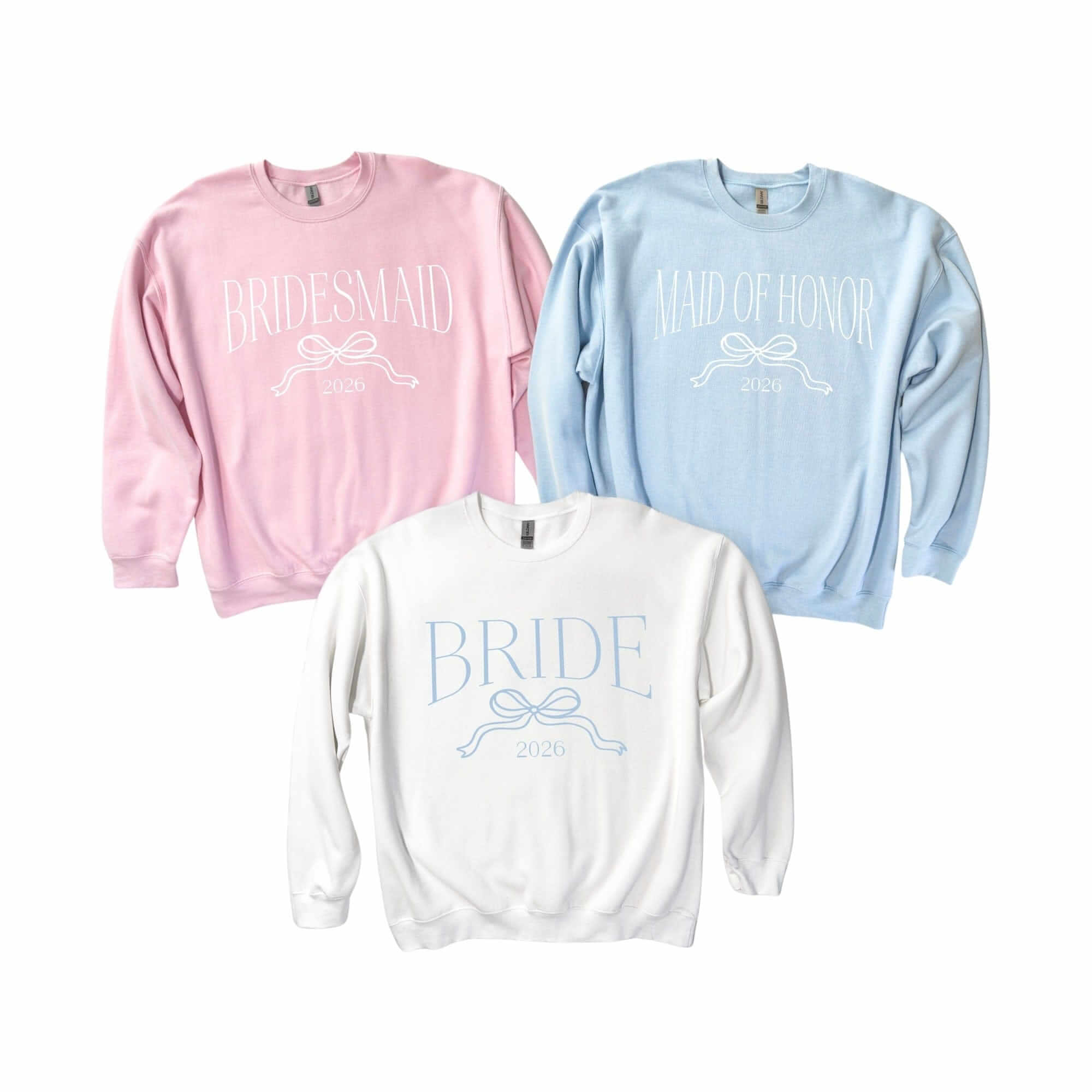 Three pastel long-sleeve crewneck sweatshirts, one pink, one light blue, and one white, each featuring a coordinated bow graphic, designed for a bridal party or wedding event.