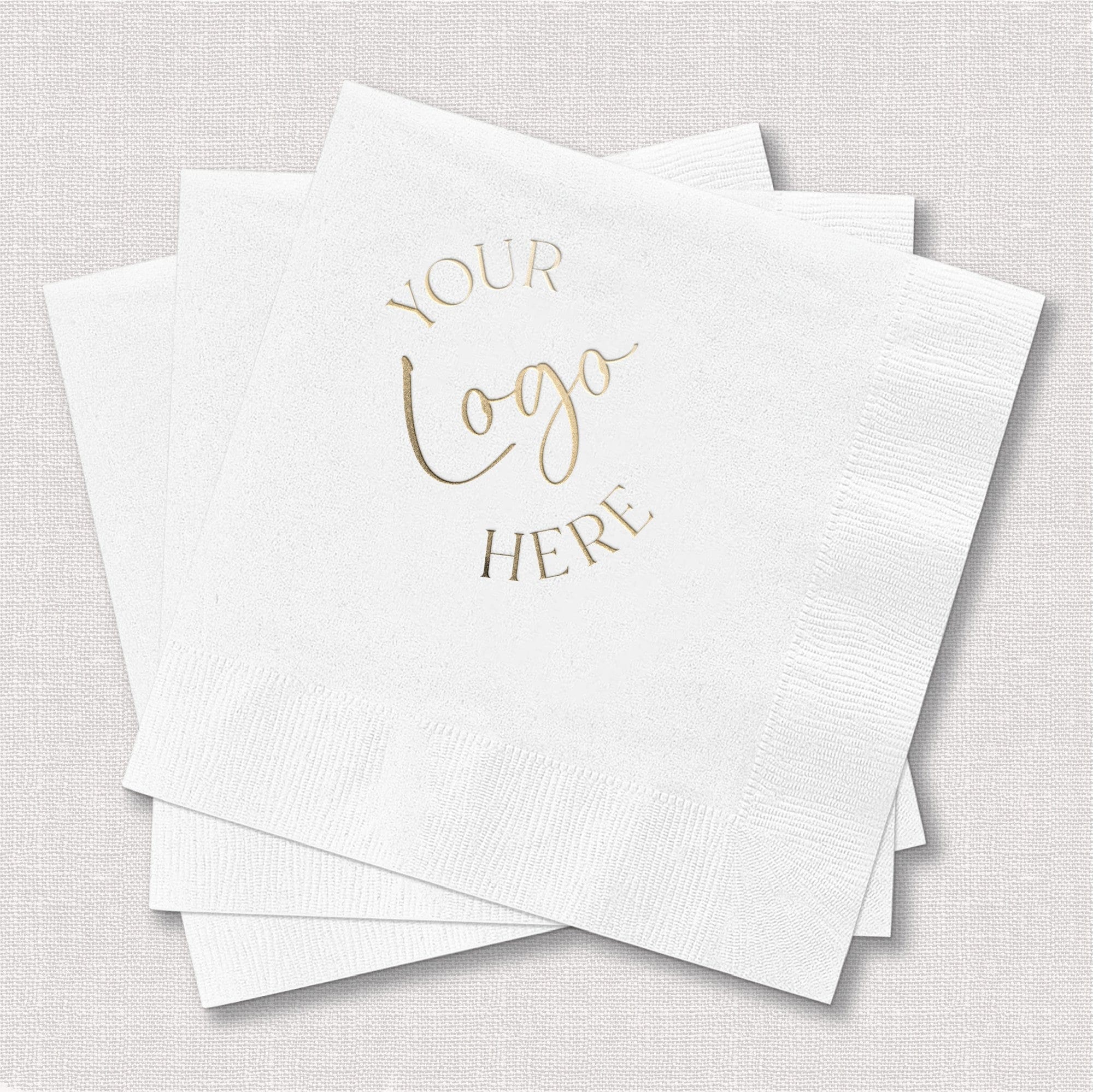 A stack of elegant white textured paper guest napkins featuring custom gold foil logo printing, ideal for personalized wedding or event decor.