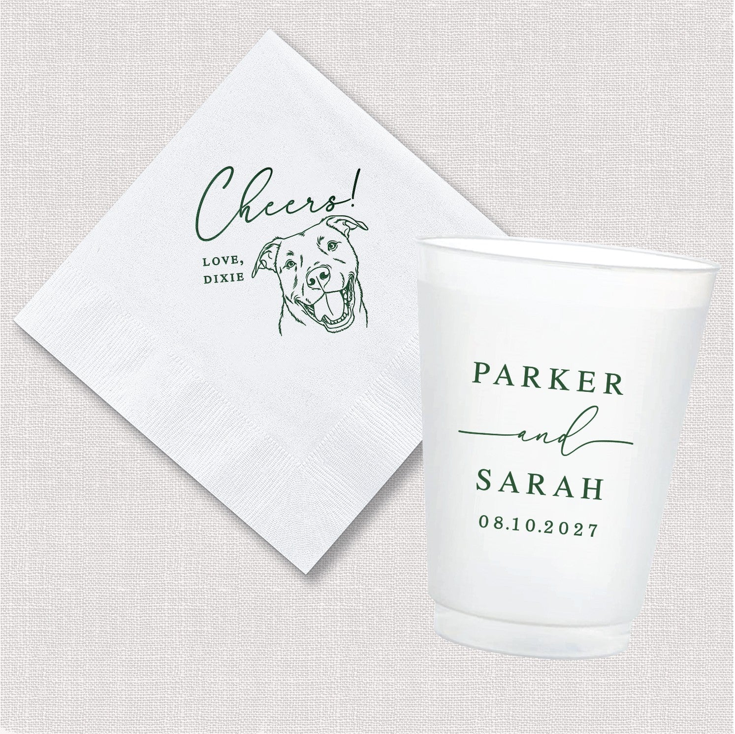 A white personalized cocktail napkin featuring green custom line art of a dog and 'Cheers!' text, paired with a white shatterproof plastic cup displaying green custom typography, suitable for a wedding or special event.