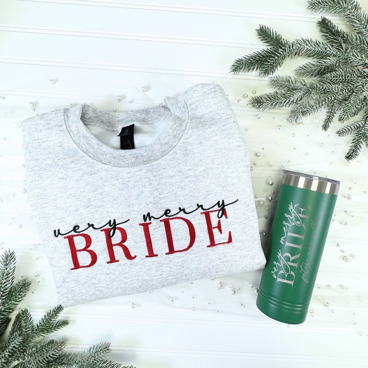 A cozy heather grey embroidered crewneck sweatshirt paired with a forest green insulated tumbler, forming a personalized gift set for a bride-to-be during her wedding journey or the holiday season.