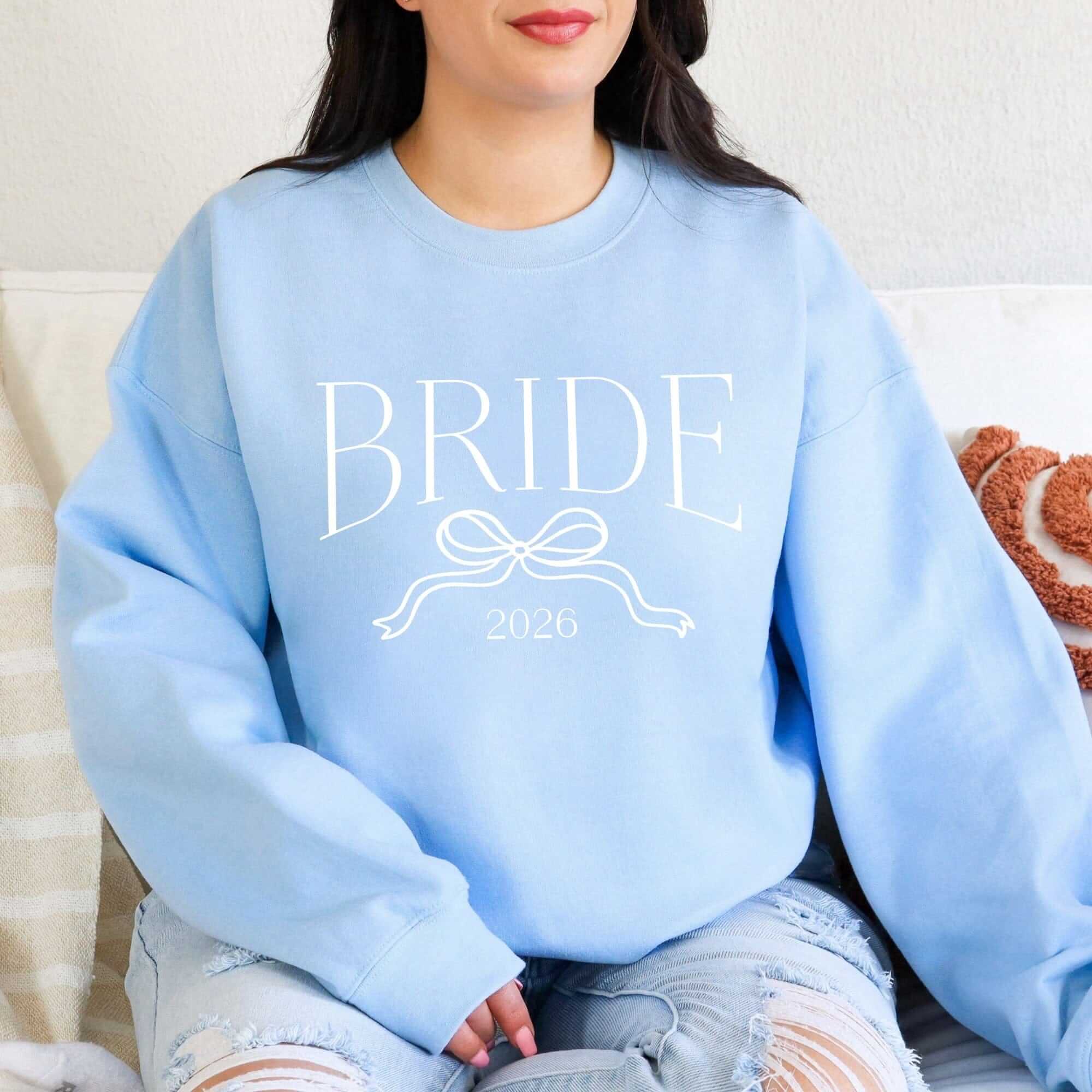 A light blue crewneck sweatshirt made from soft fabric, featuring a white graphic of a bridal term above a decorative ribbon design, suitable for wedding events.