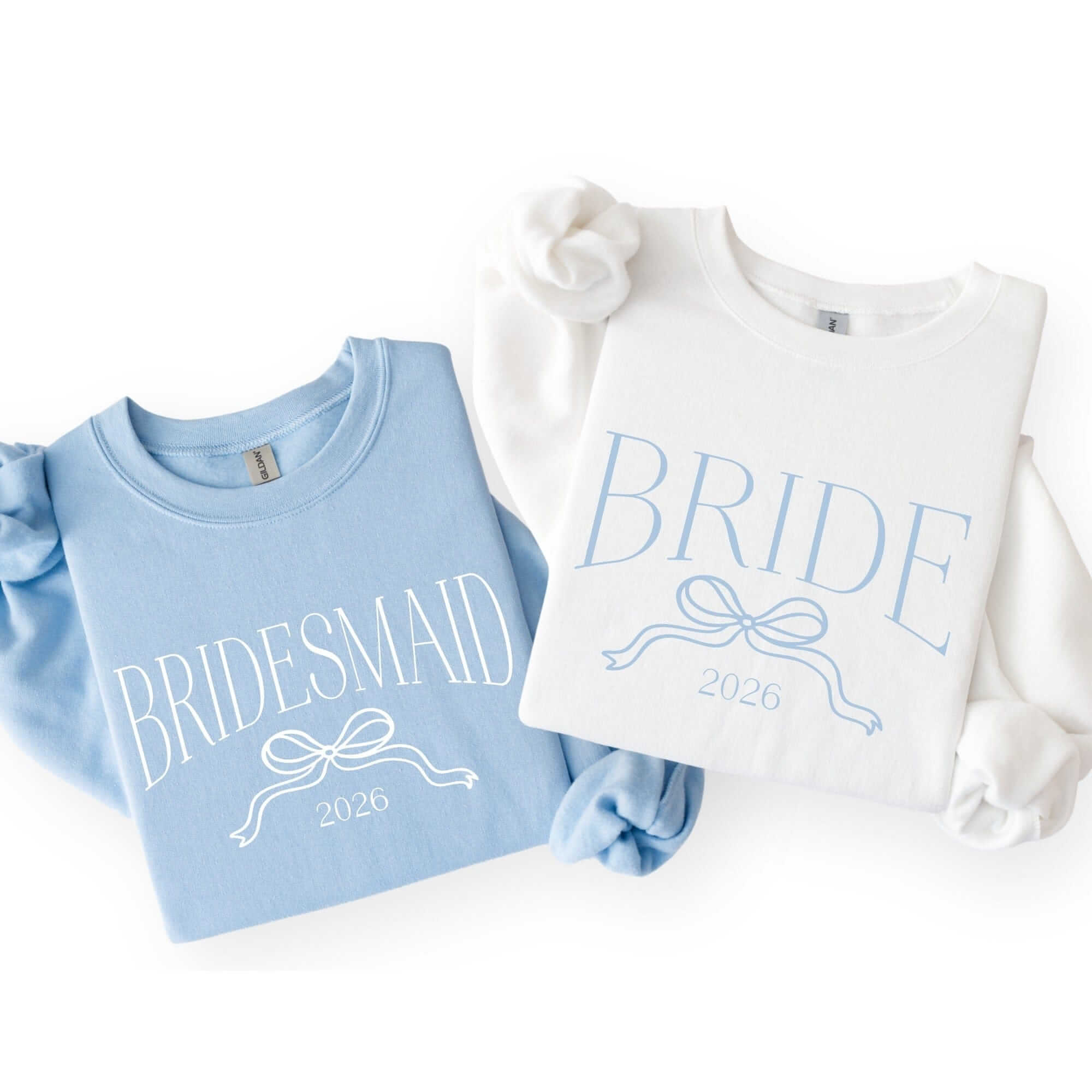 Two fabric crewneck sweatshirts, one light blue and one white, each featuring a complementary ribbon graphic, perfect for bridal party wear.