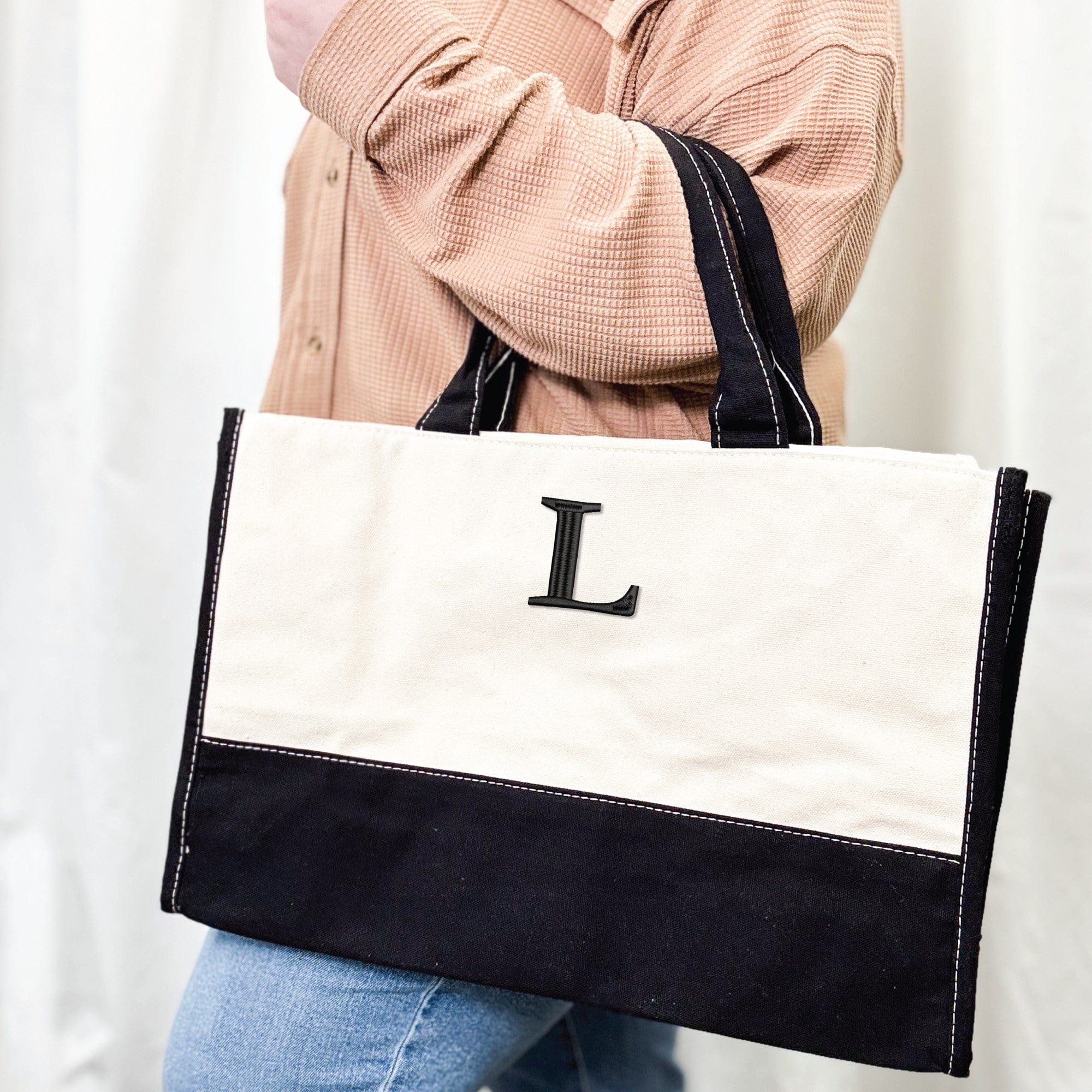 A two-tone canvas tote bag with a natural top section and a black bottom section, featuring sturdy black handles with white accent stitching, perfect for carrying essentials or as a personalized accessory.