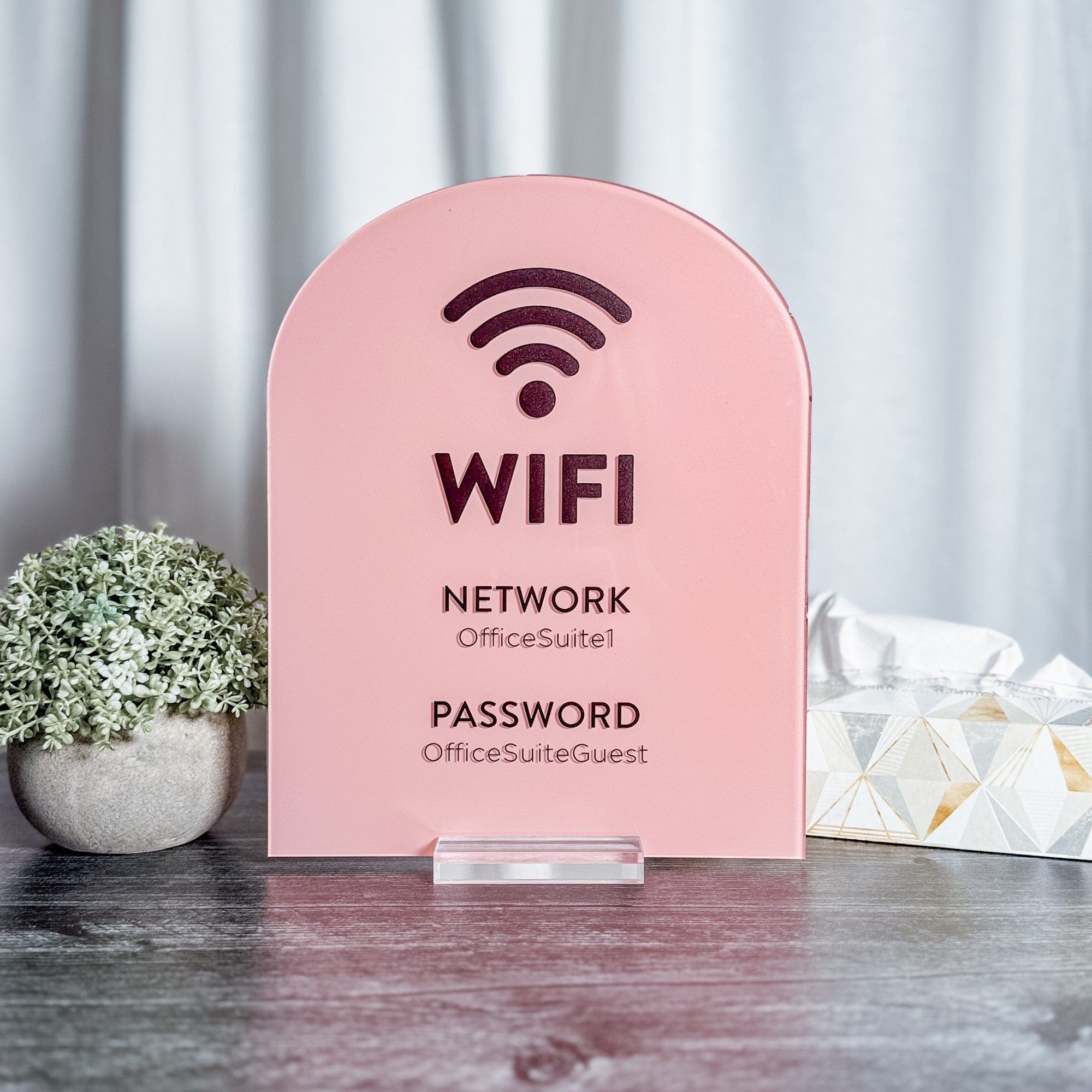 A pink arched acrylic sign with a clear stand, designed to display Wi-Fi network and password information for guests at an event or business.