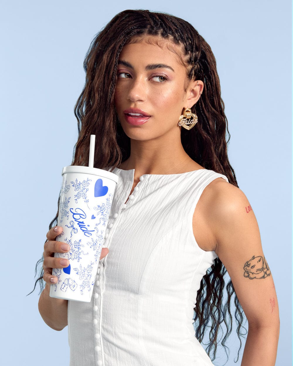 Woman holding white 24 oz tumbler with blue floral design and straw against light blue background